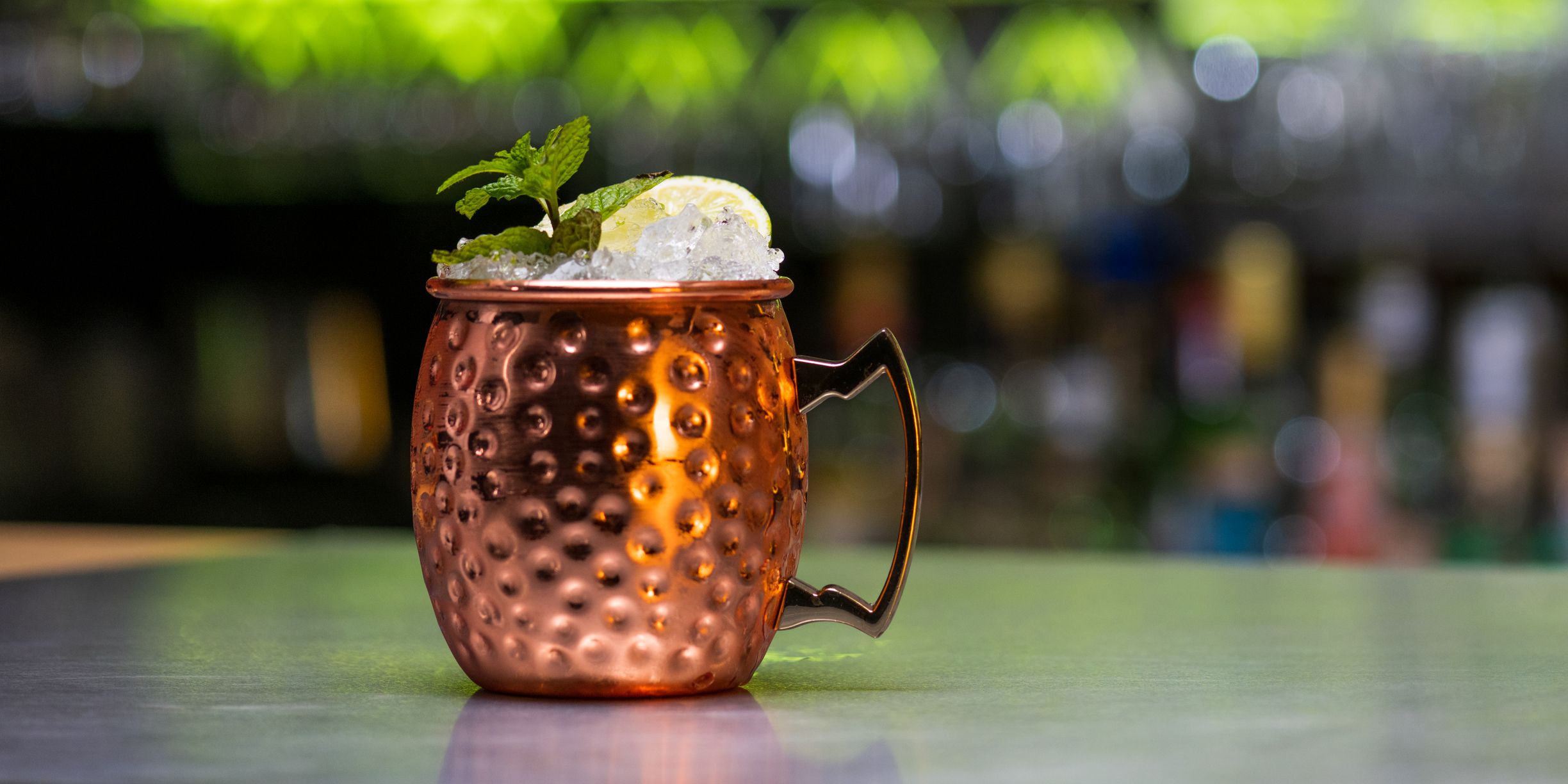 Close-up of Moscow mule drink with ice cubes, lemon slice and mint leaves on table in bar.