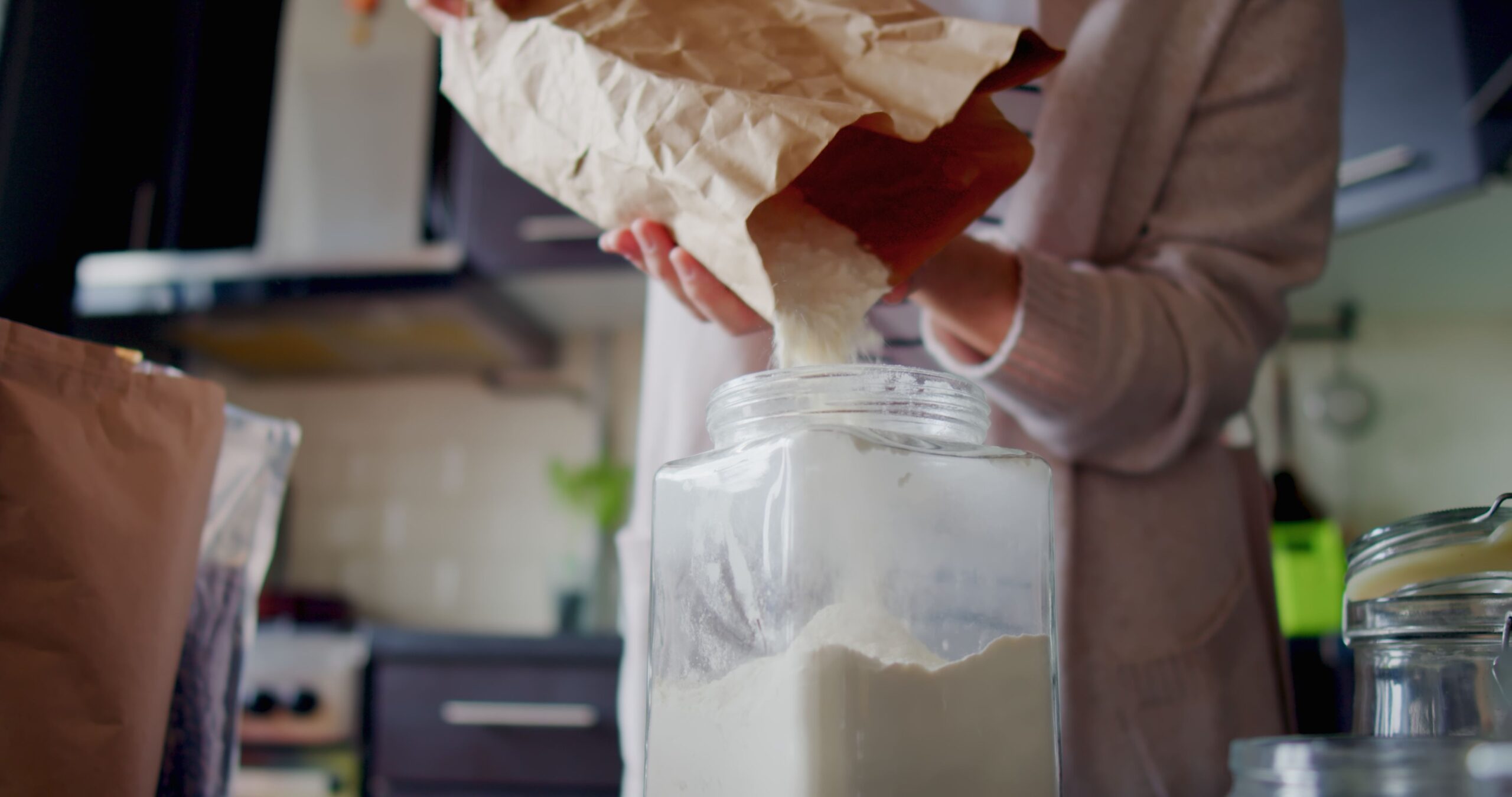 Woman is organizing food in her kitchen pantry. She aims to stop using plastic at home, so she uses glass containers for food storage