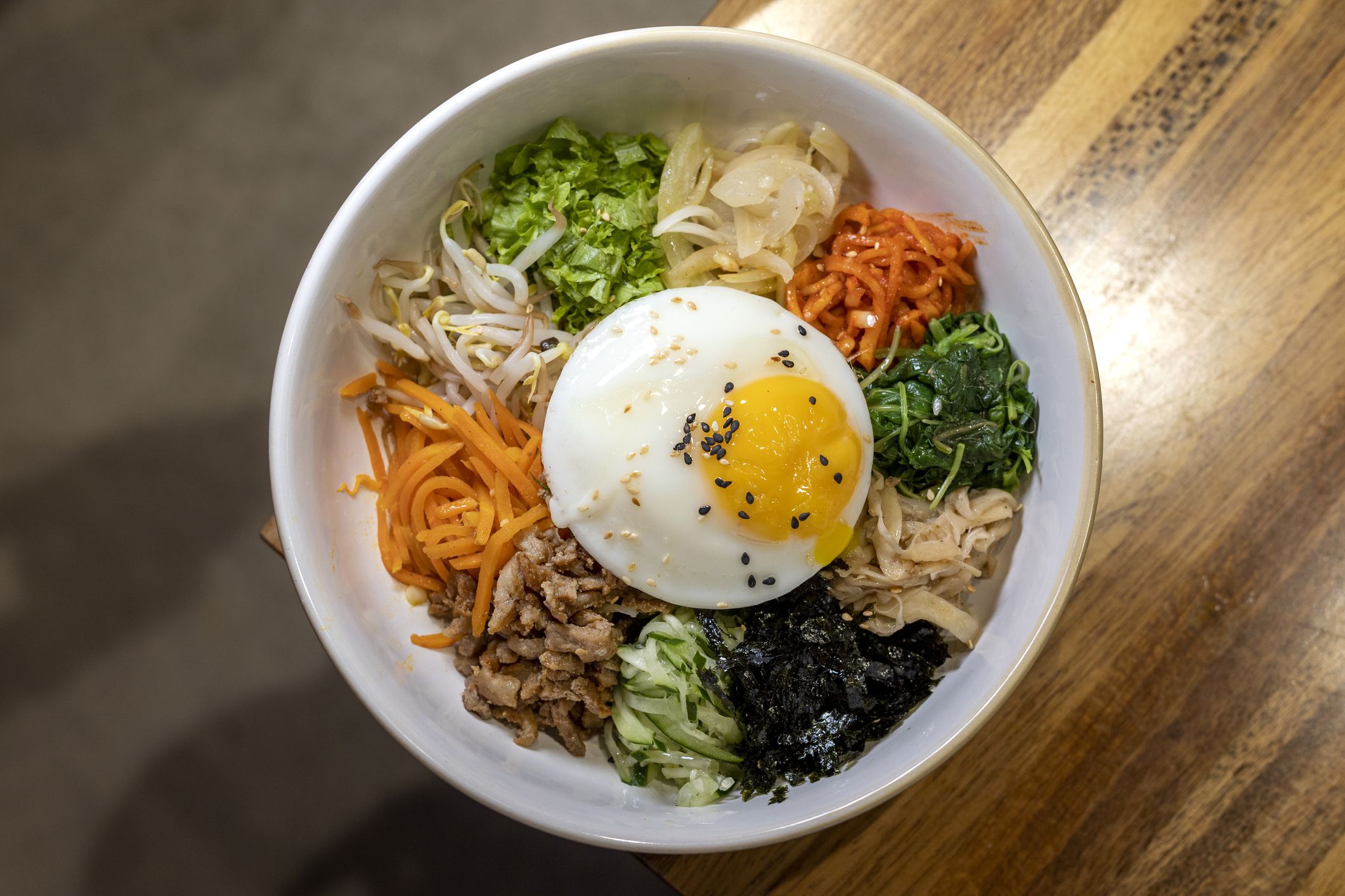Bibimbap is served as a bowl of warm white rice topped with namul or kimchi and gochujang, soy sauce, or doenjang