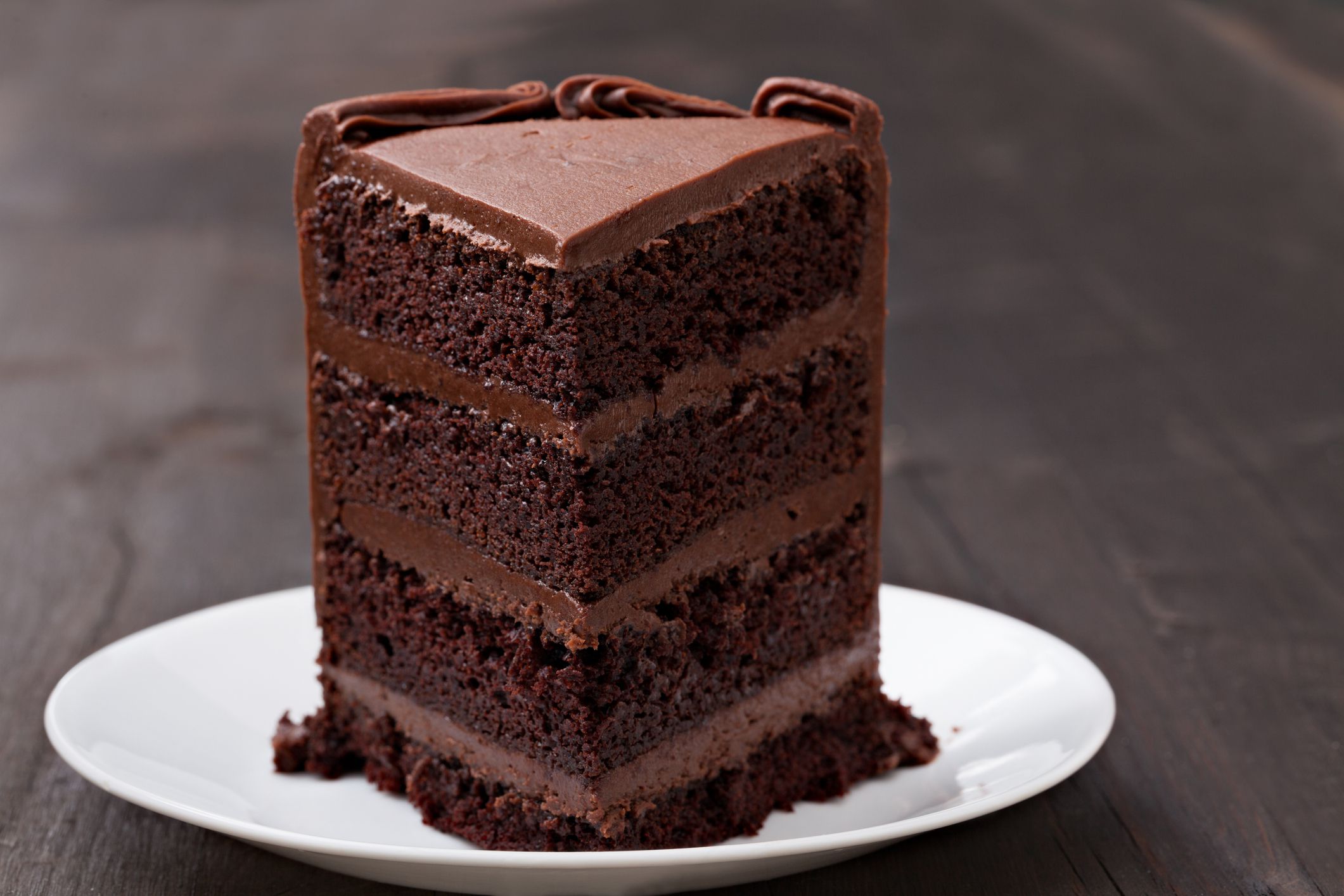 An extreme close up photograph of a generous slice of chocolate fudge cake on a white plate.