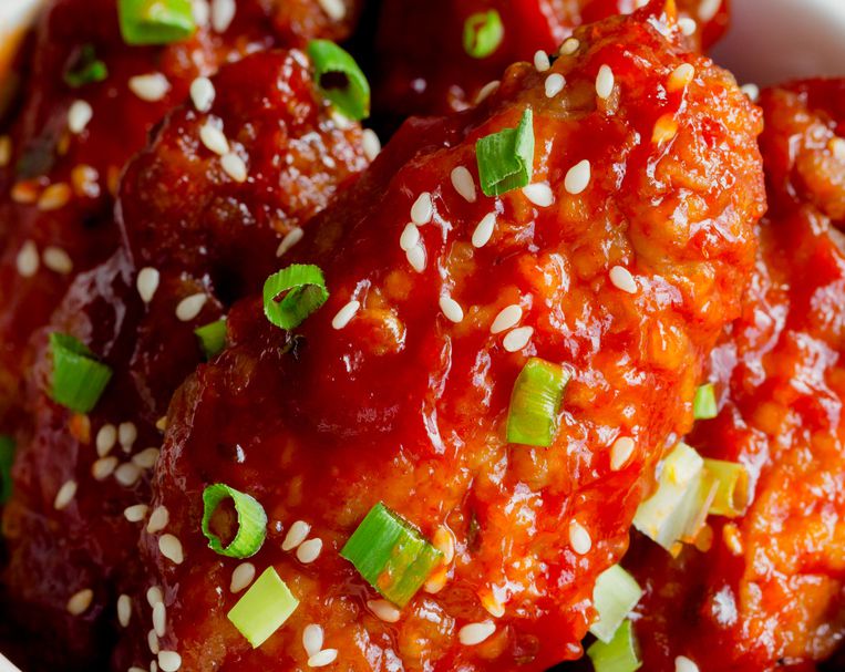 Korean fried chicken wings sprinkled with sesame and spring-onion on wood plate. Korean barbecue chicken wing delicious,moist and spicy. Close up on fried chicken wings in Korean style on wood table.