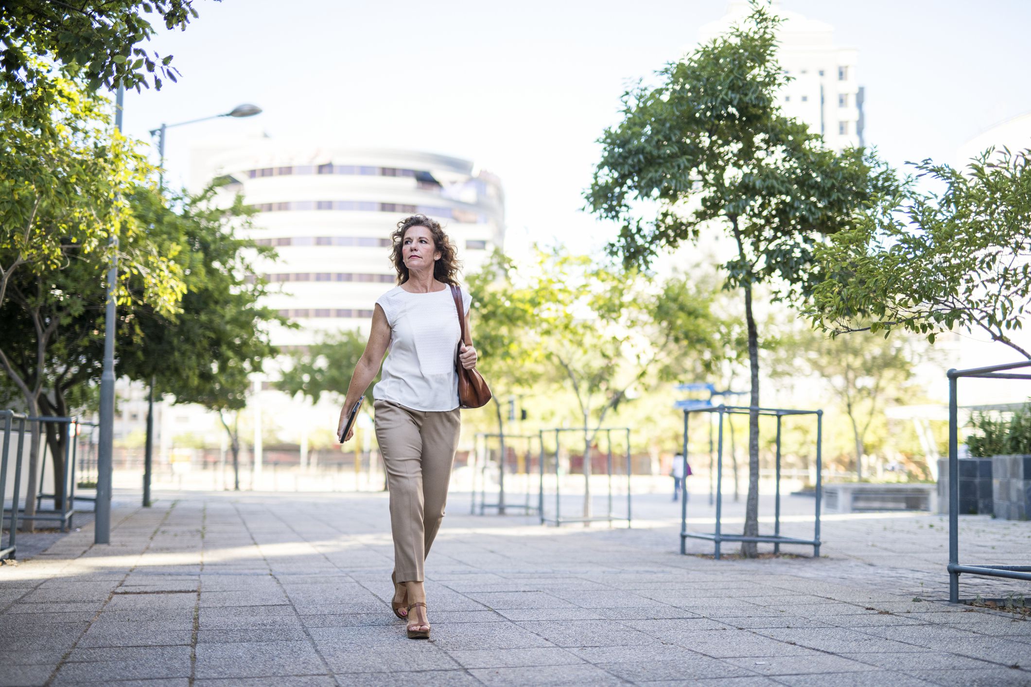 Full length of mature businesswoman walking on footpath. Female professional is looking away in city. She is wearing smart casuals.