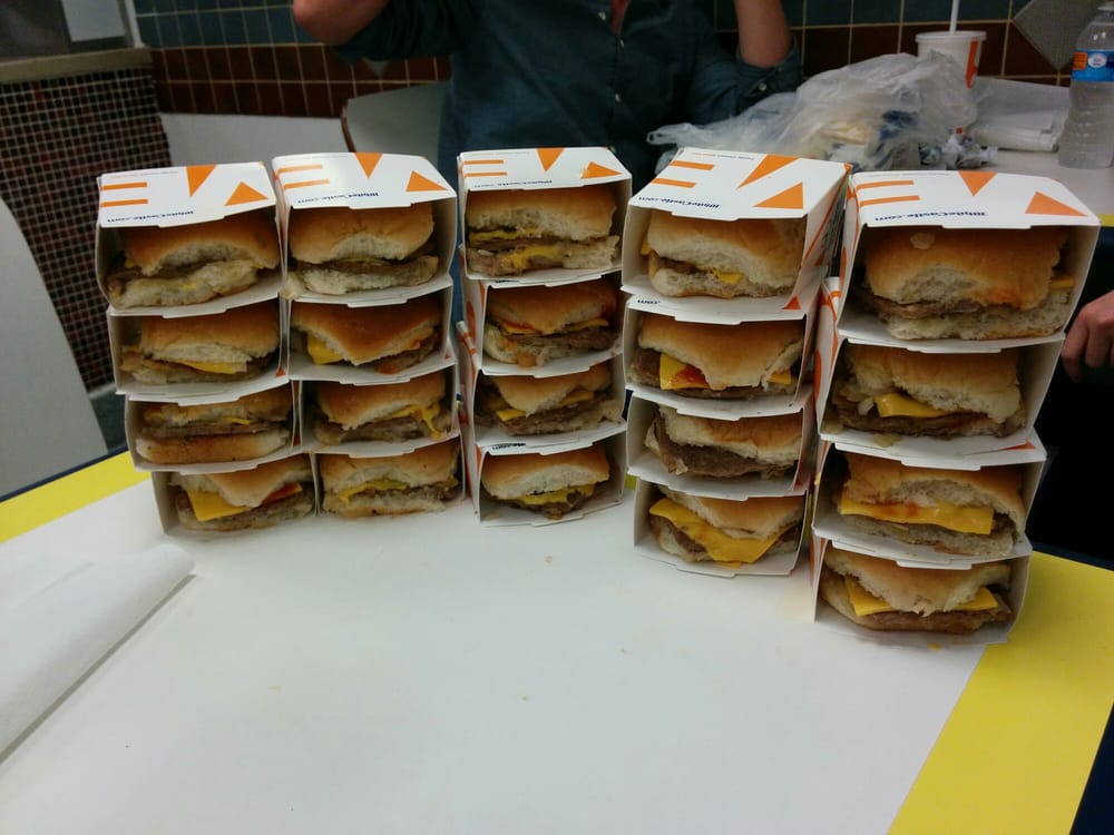 Stacks of cheeseburgers still in their open cardboard boxes are arranged in rows on a table, with a person partially visible in the background.