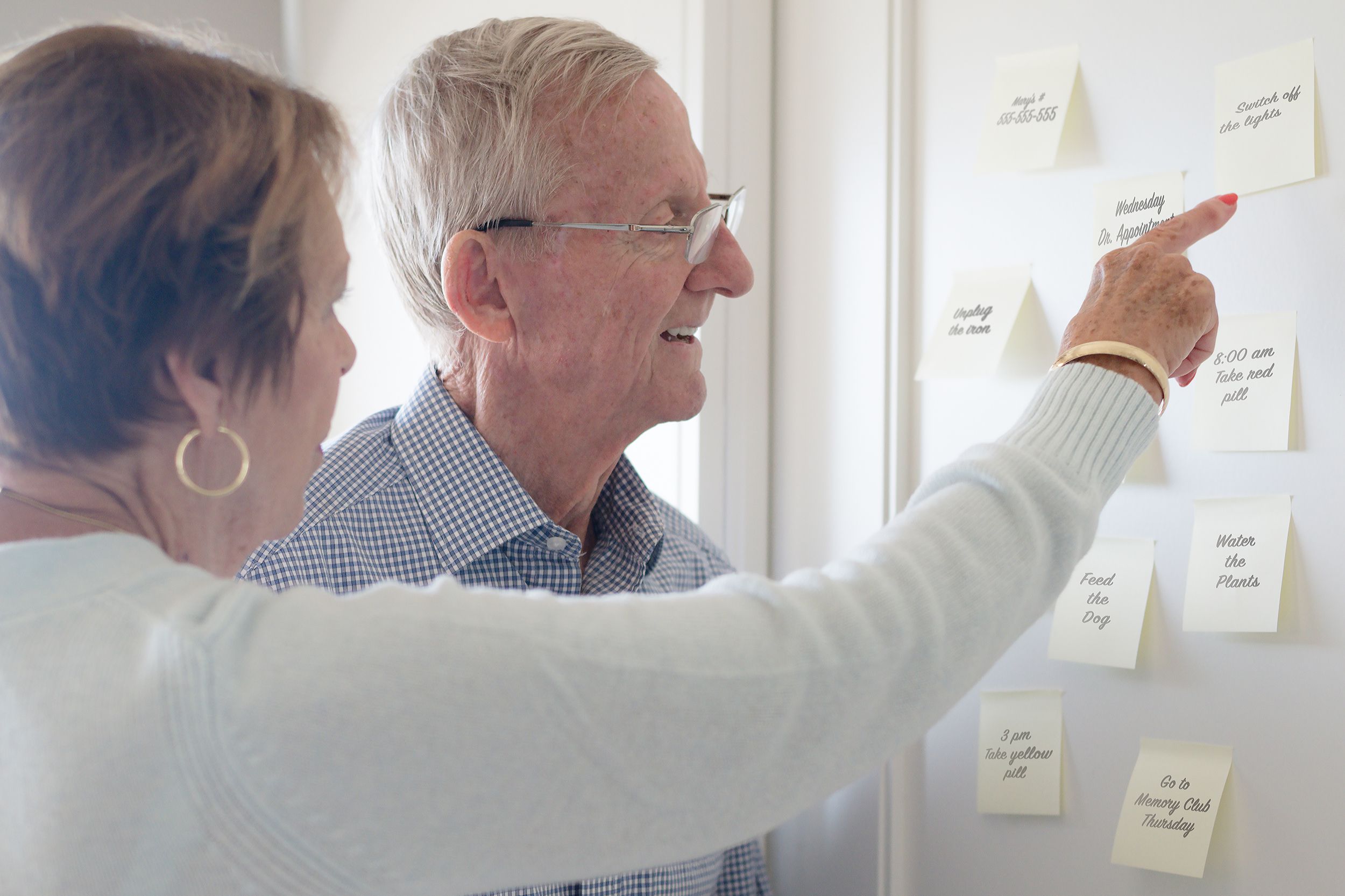 middle-aged woman pointing to stickie notes for senior man with dementia