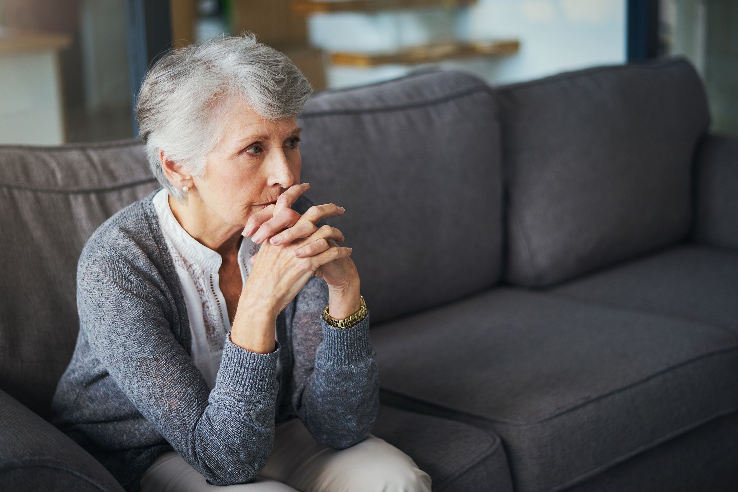 anxious senior woman sitting on her couch, thinking