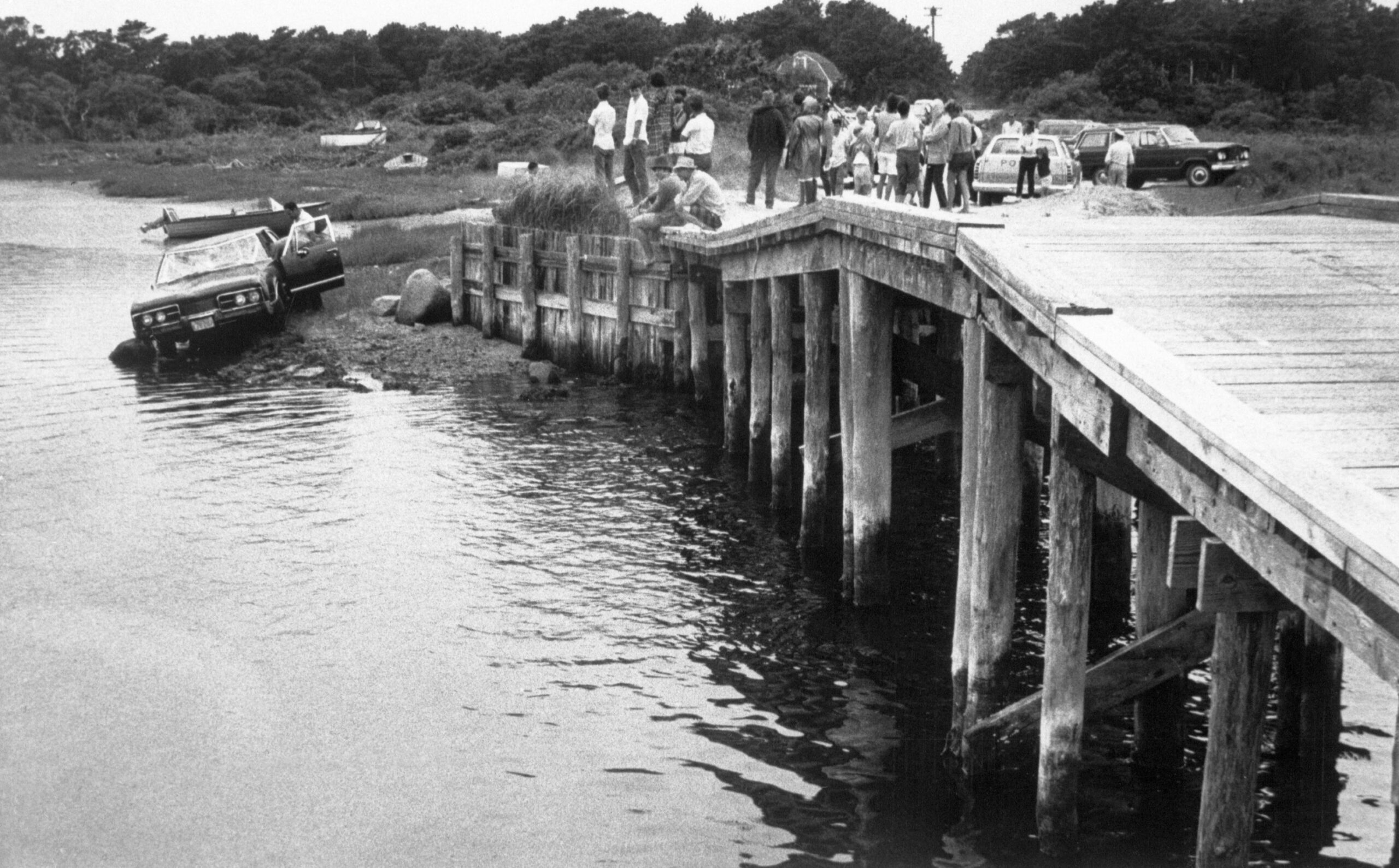 Curious spectators look on from pier at the car driven by Massachusetts Senator Edward Kennedy which plunged off a bridge on Martha's Vineyard on July 19th.