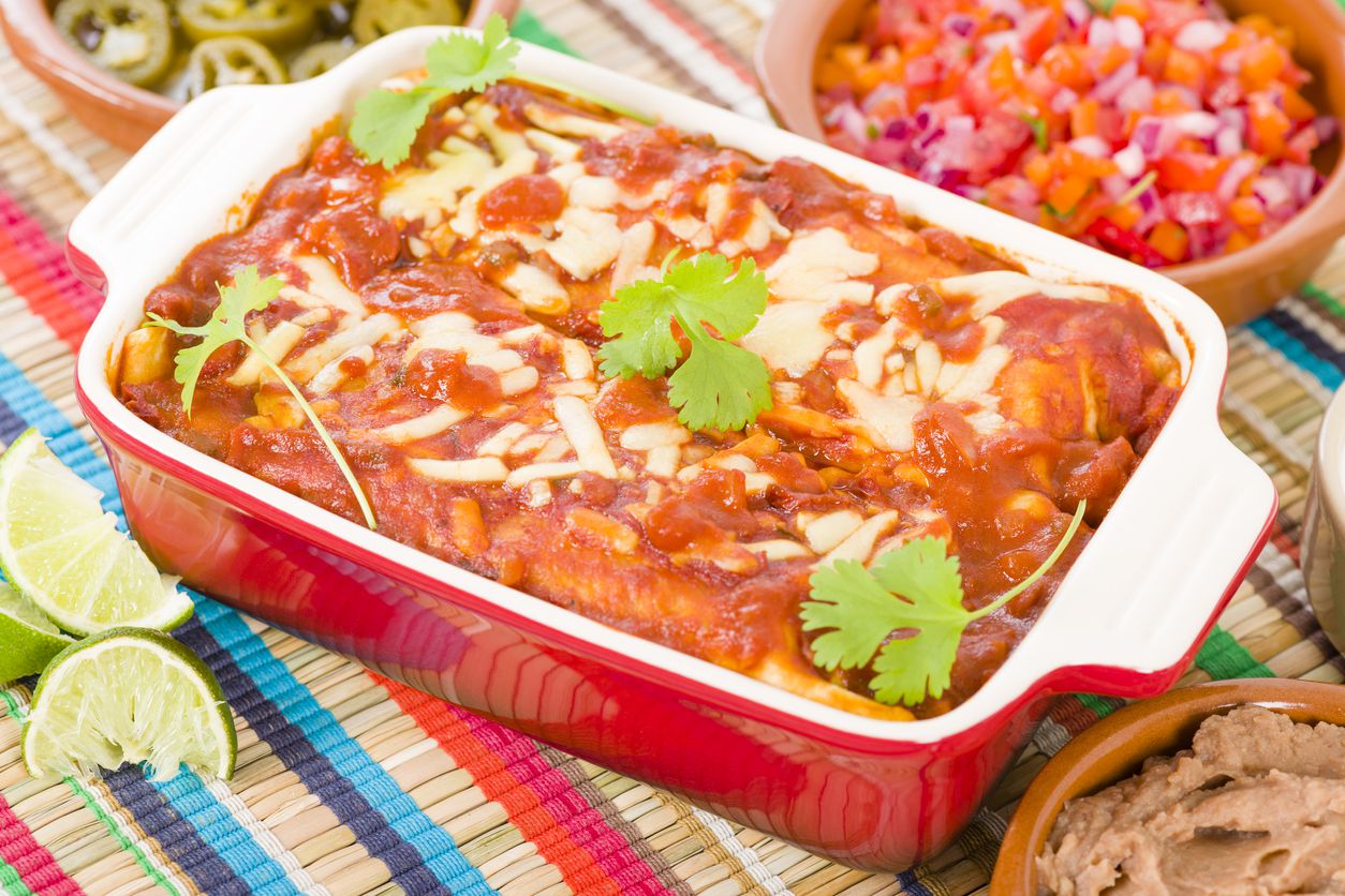 Chicken & Chorizo Enchiladas casserole with cilantro leaves in a red ceramic baking dish with salsa and dips