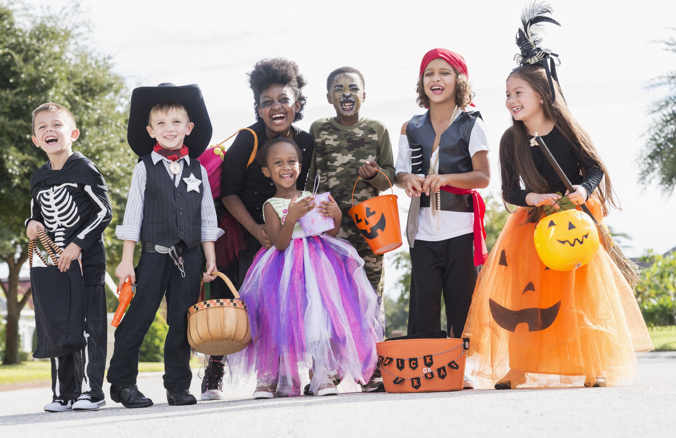 A multi-ethnic group of seven children wearing halloween costumes. They are mixed ages, from 3 to 10 years old, ready to go trick or treating.