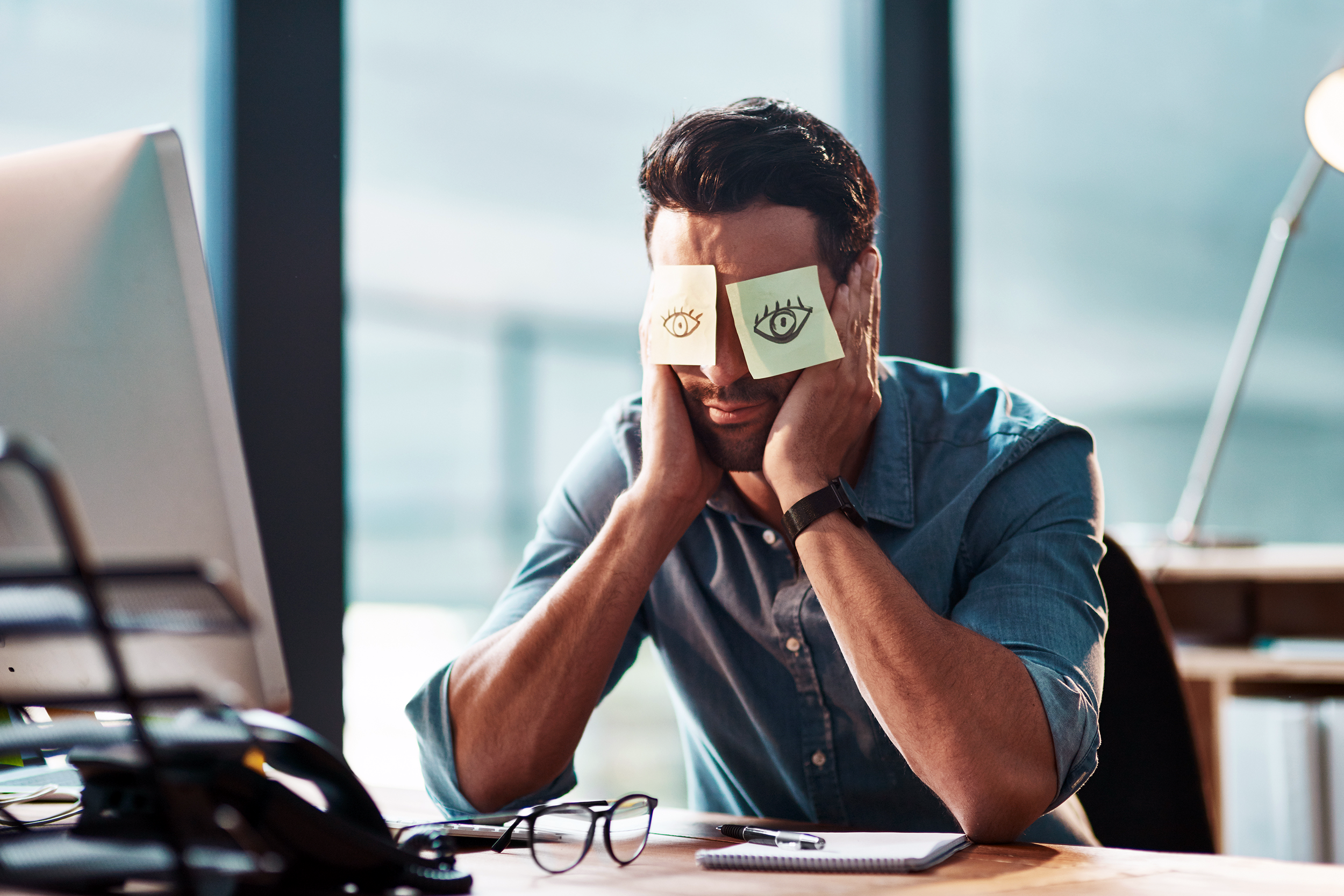 Man sleeping at his desk with Post-It notes over his eyes