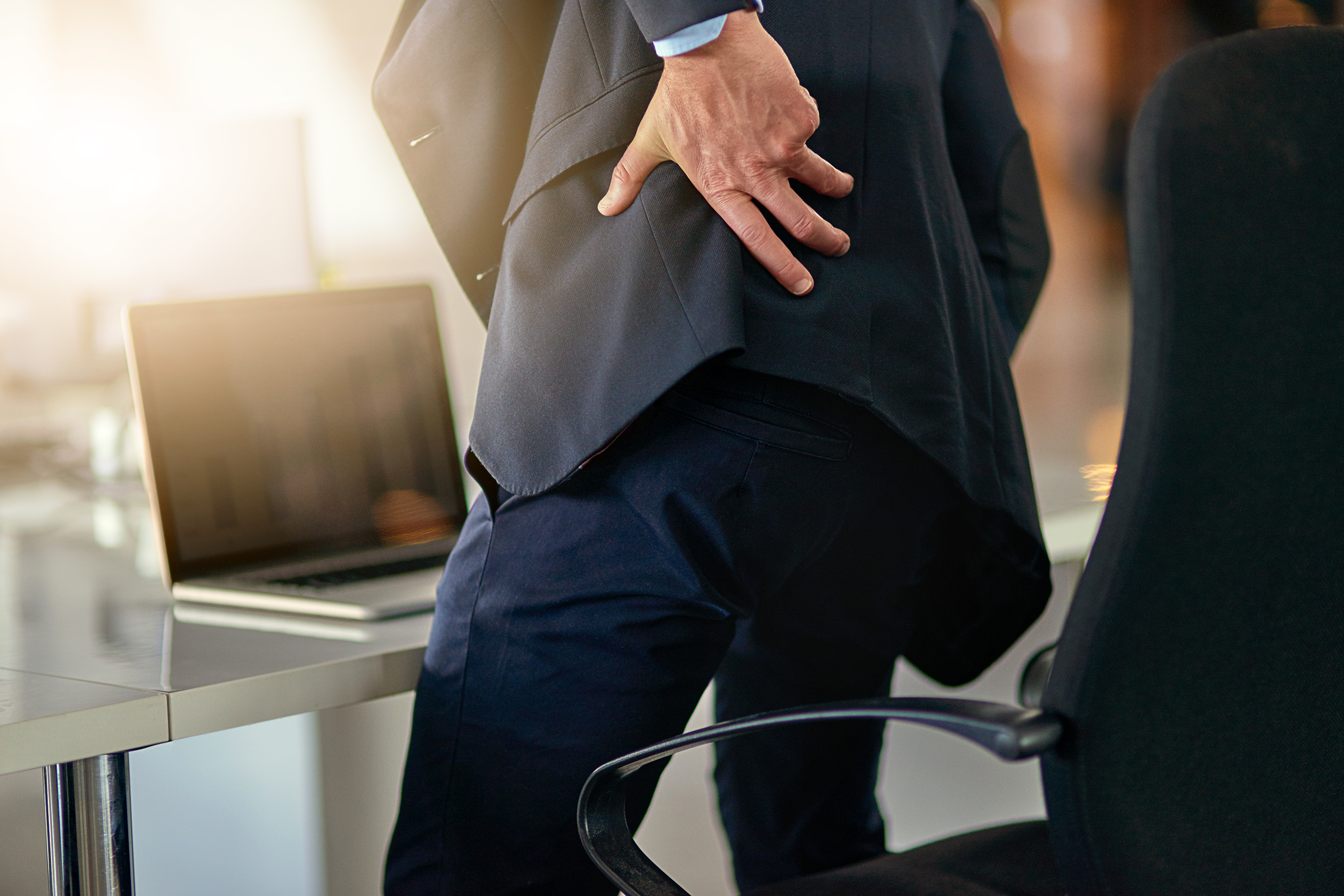 Man at work standing up from his desk and holding his back in pain