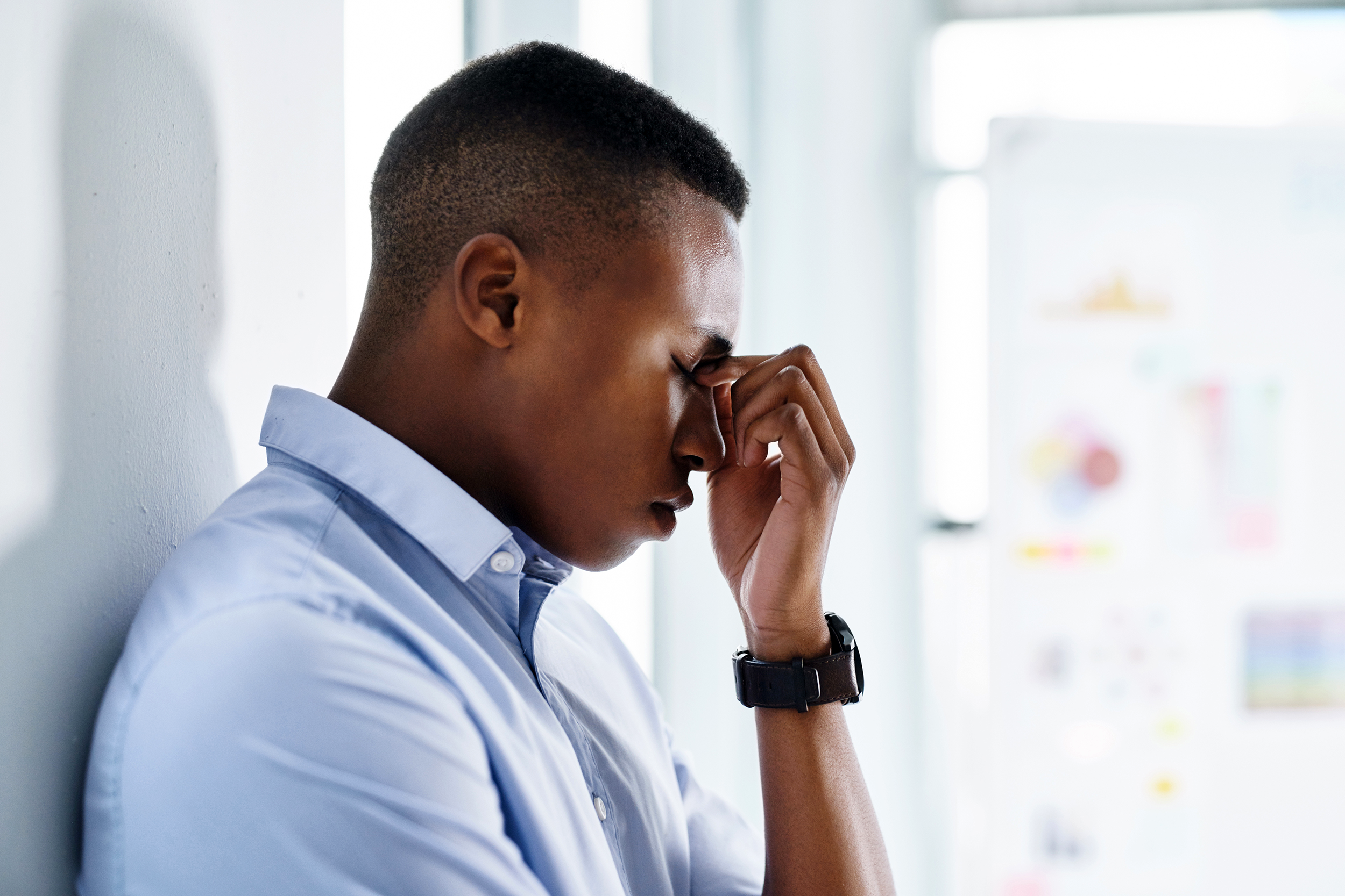Young man at work standing against a wall with his hands on his face looking distraught