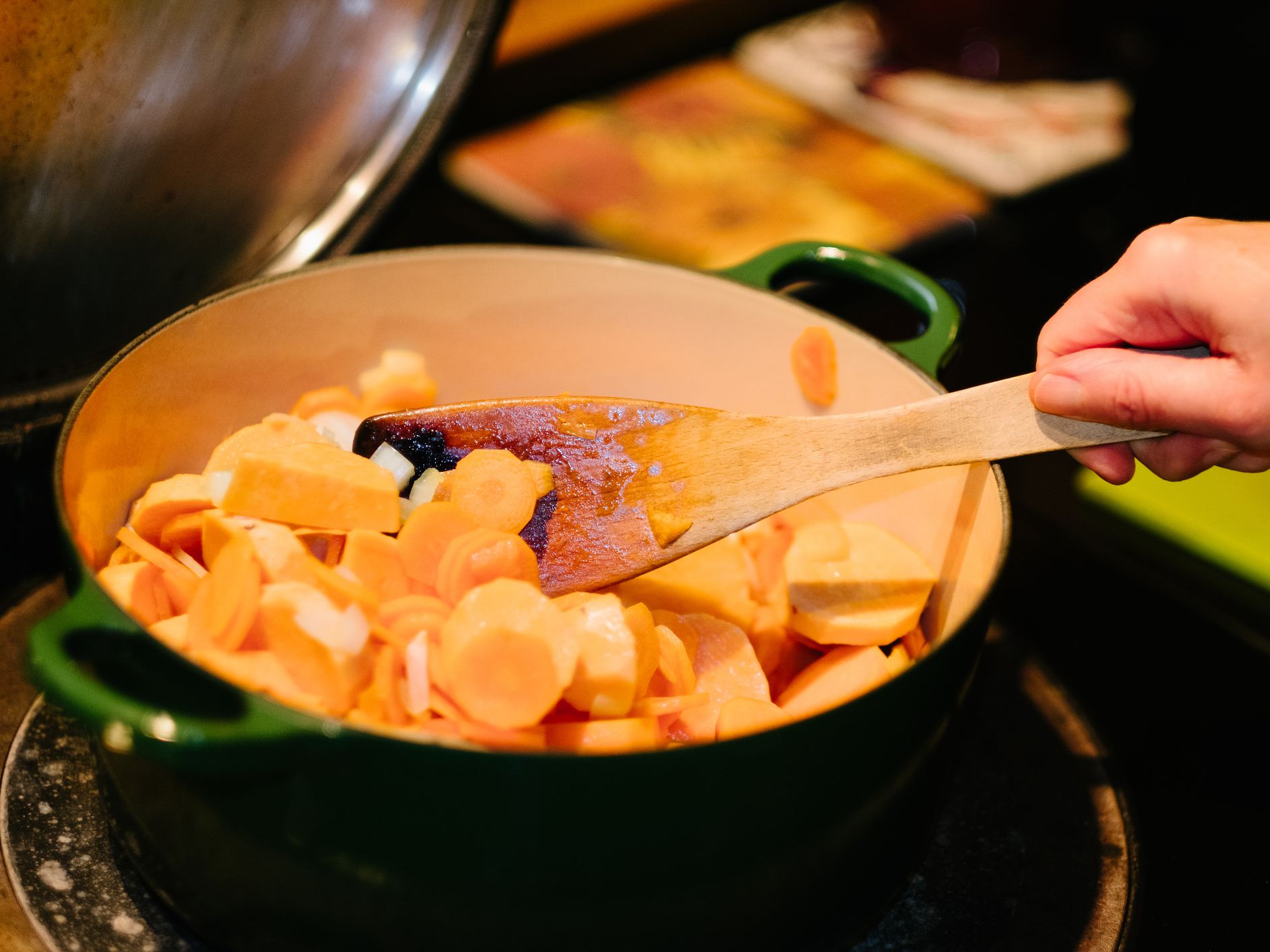 Gently frying chopped sweet potato and carrots in a cast iron pot on a stove.