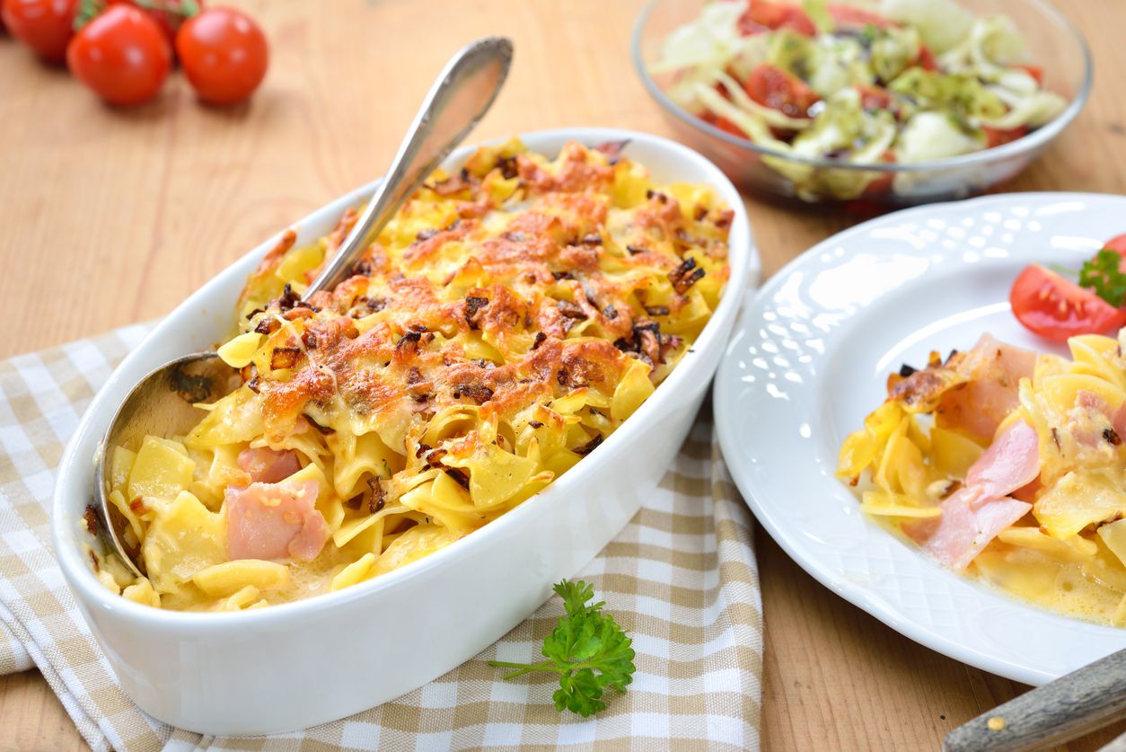 Schinkenfleckerl casserole in an oval white baking dish on a white and beige checkered napkin