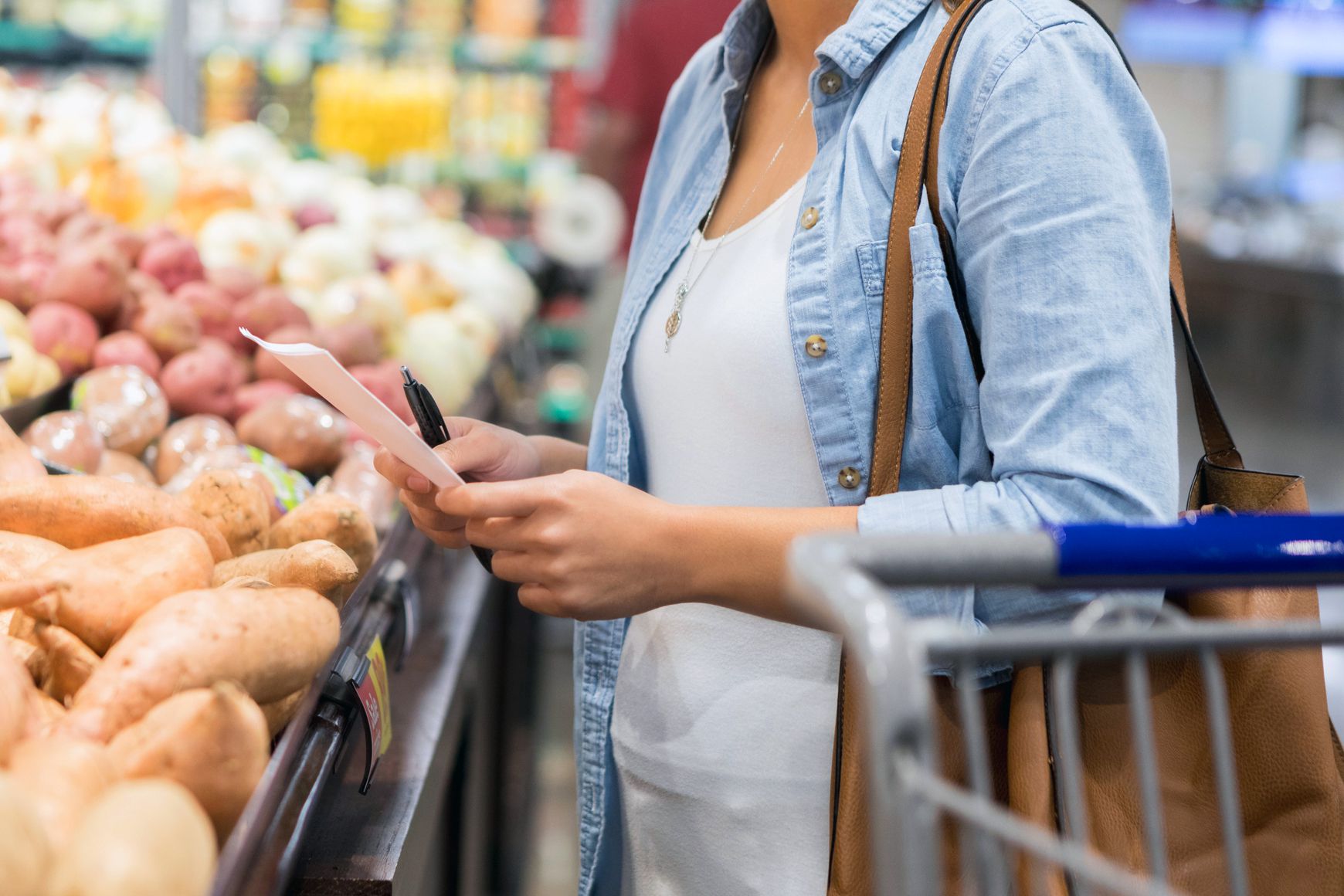 woman at grocery store with pen in hand looking at grocery list, produce aisle