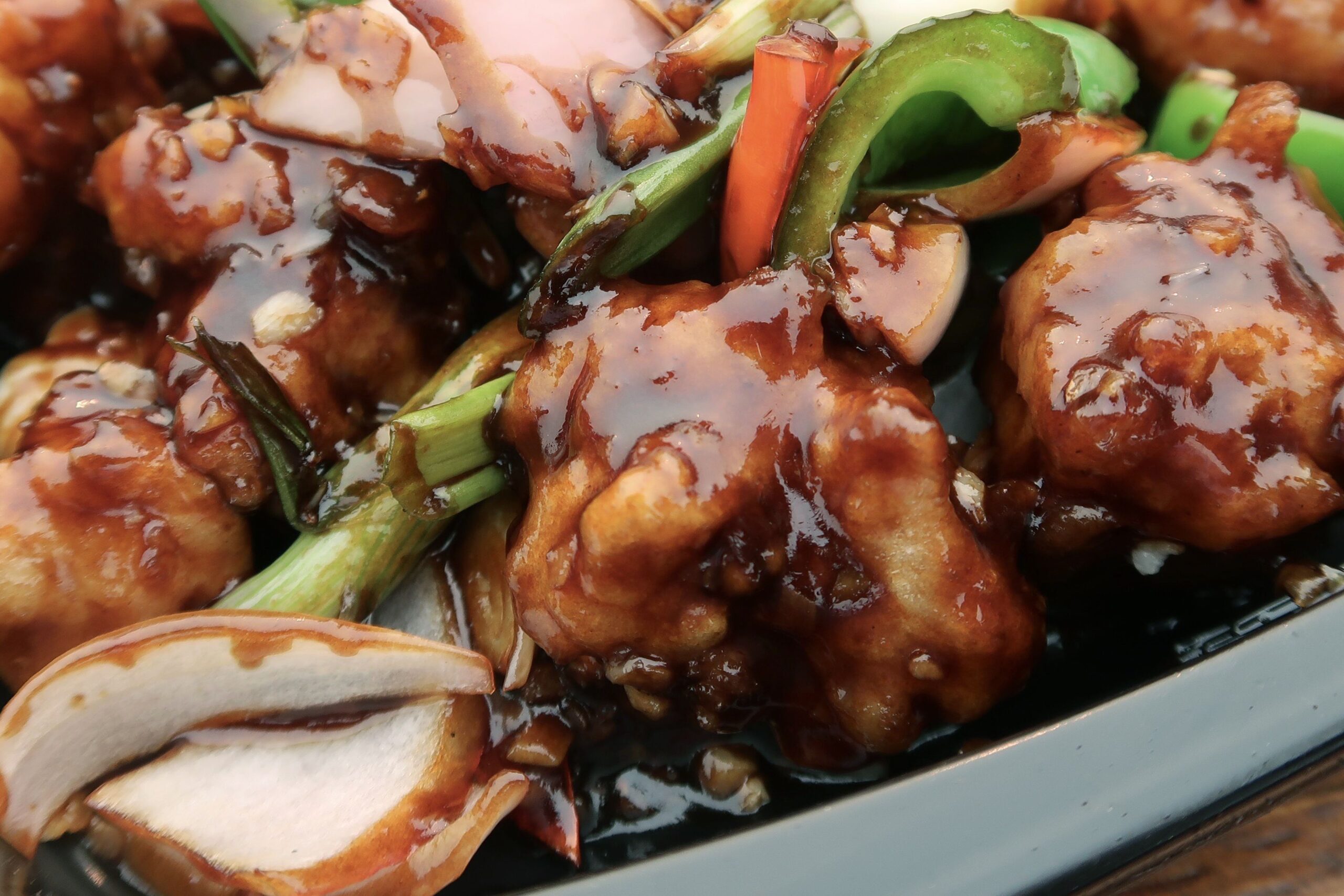 Stock photo showing a take away meal of spicy Kung Pao Chicken in a black plate disposable container with wooden chopsticks.