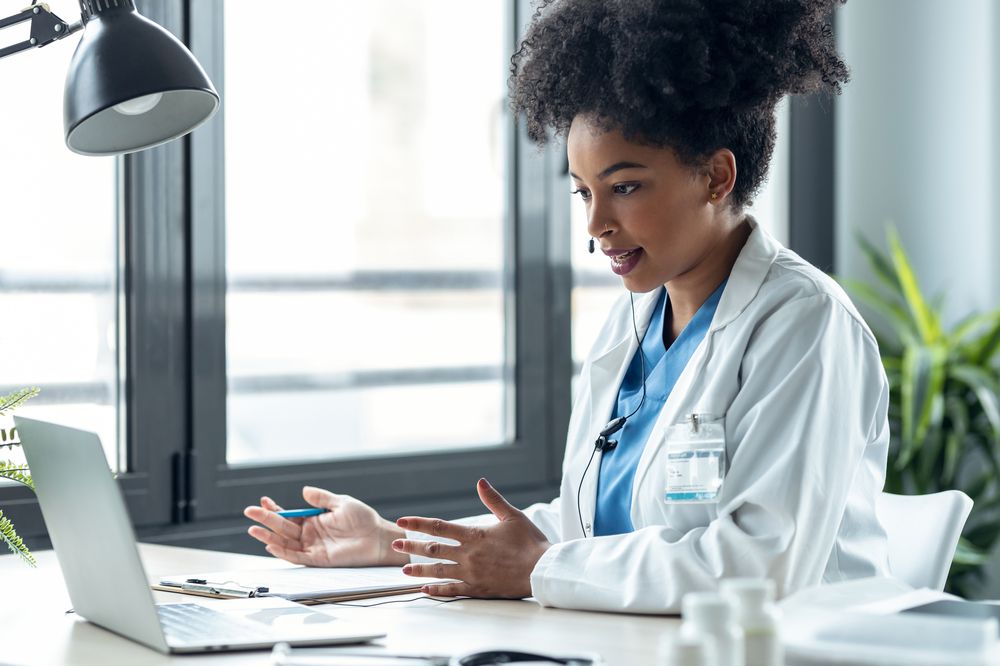 Attractive afro female doctor talking while explaining medical treatment to patient through a video call with laptop in the consultation.