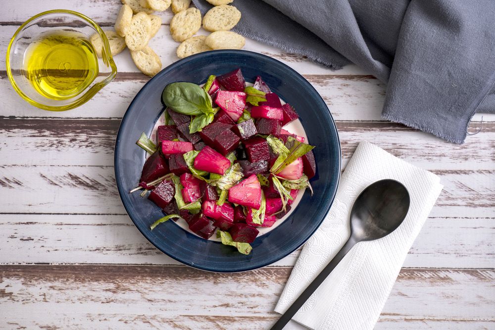 Beet, pineapple and chicory salad with olive oil and basil on a plate on a rustic table in still life style. Fresh and healthy vegetables concept.