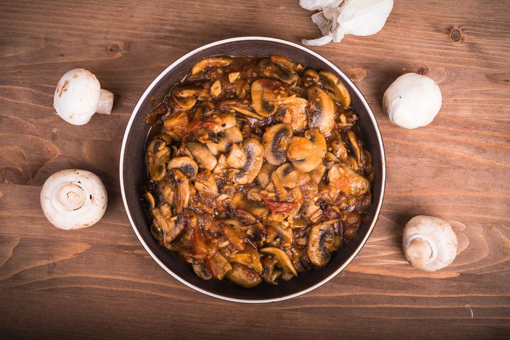 Homemade stew of tomatoes and champignon mushrooms in a plate on the table, top view, close-up