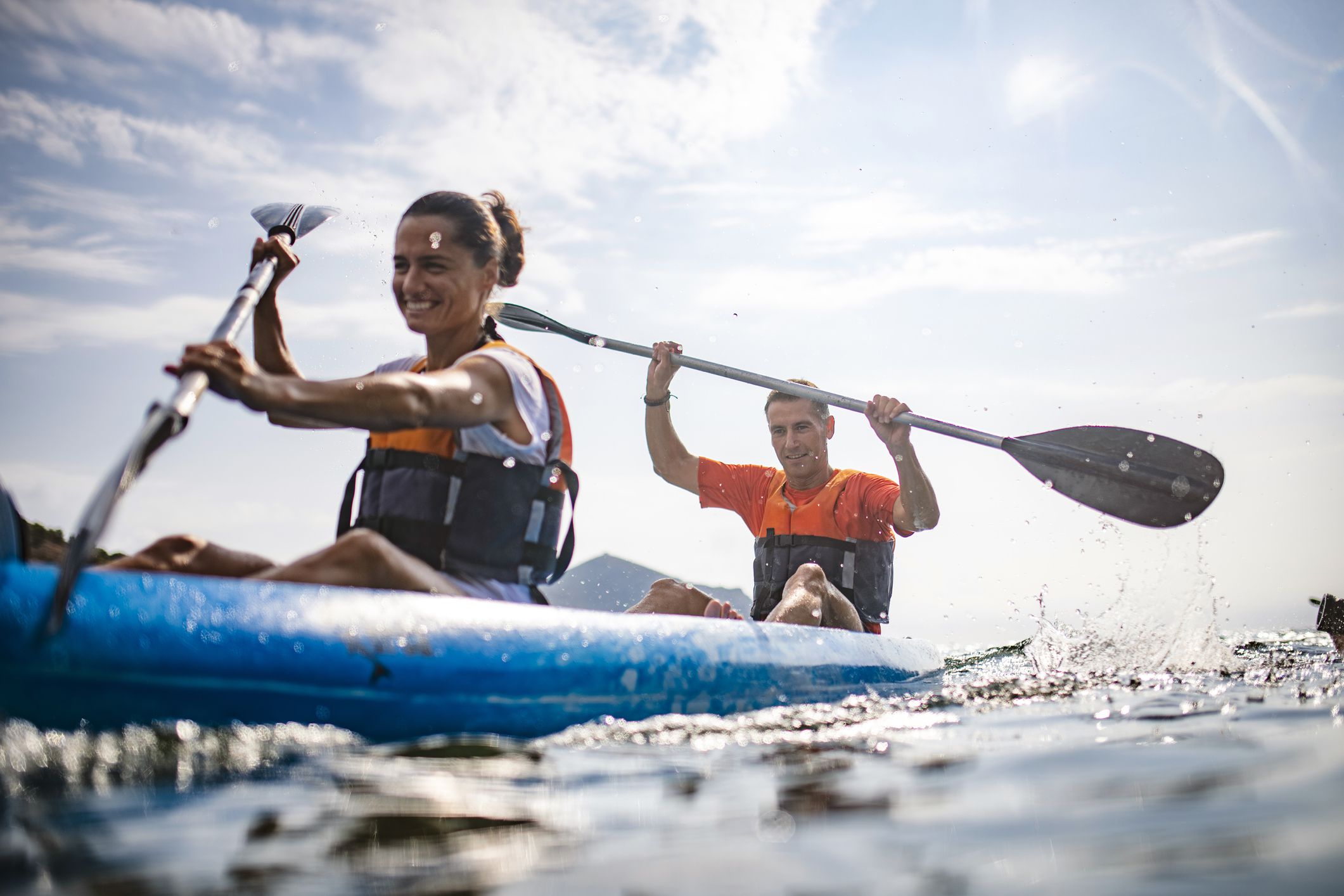 Water surface level view of energetic male and female kayakers in 30s and 40s paddling past camera in Mediterranean Sea off the Costa Brava.