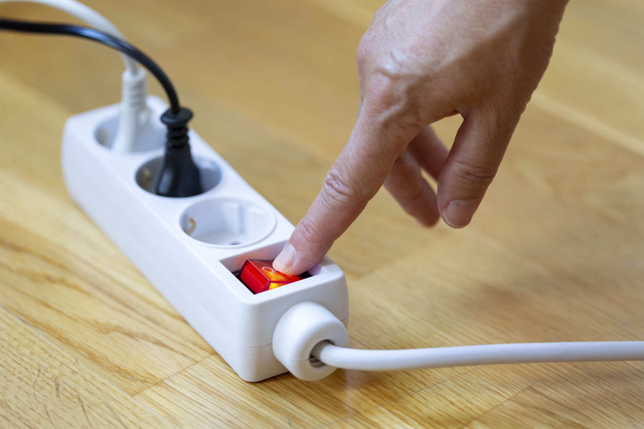 Pressing red button of a white power strip on wooden background - energy saving