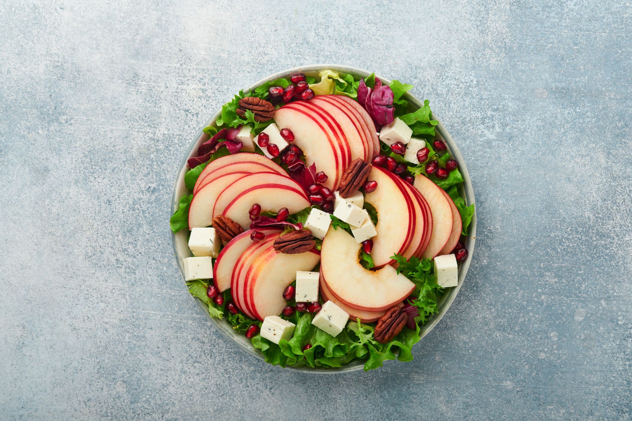Salad. Fresh fruit green salad with feta cheese, apple, pomegranate, pecan and lettuce on white plate. Idea for healthy delicious winter Christmas salad. Healthy balanced eating. Top view.