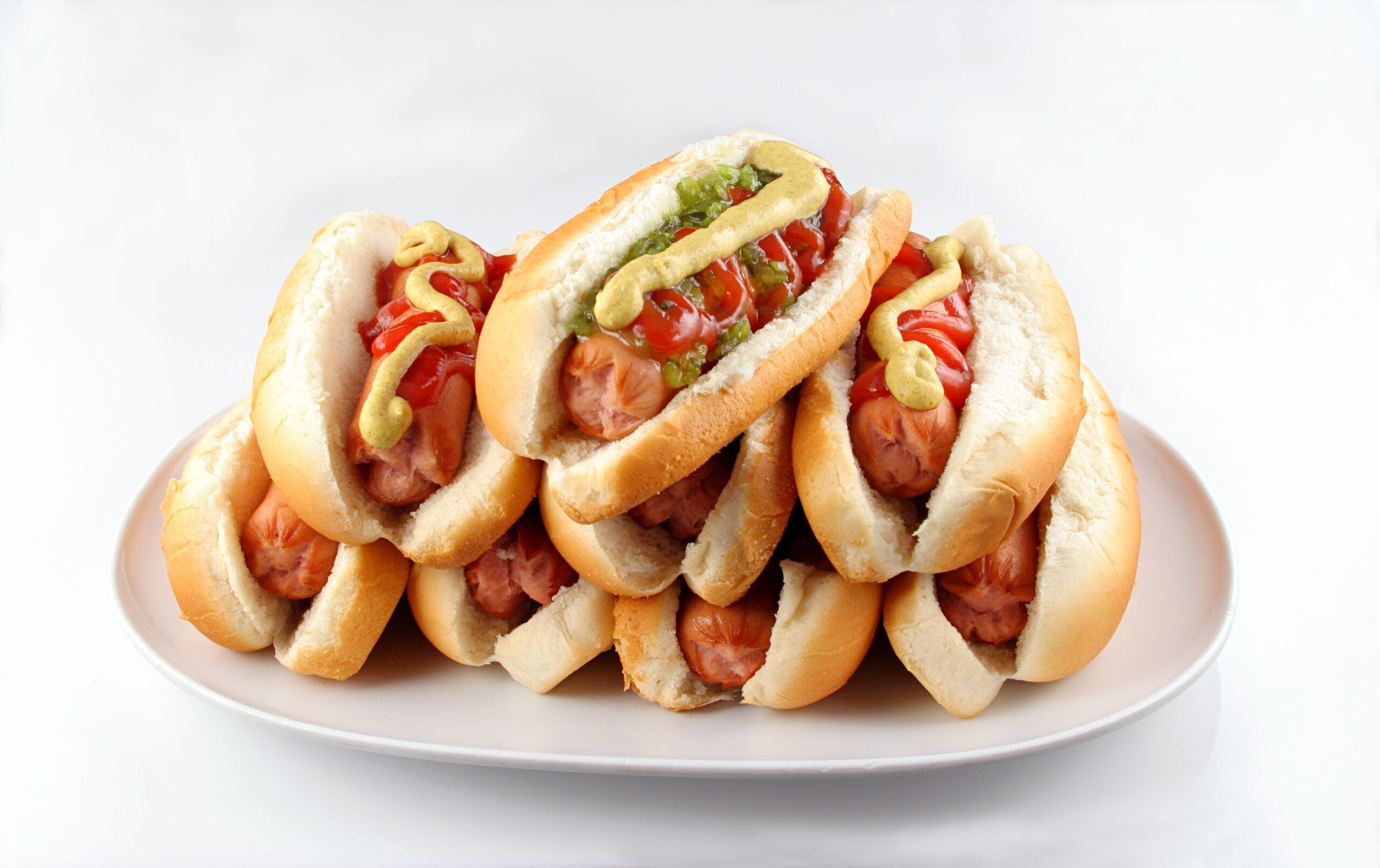 Plate of stacked hotdogs. Ketchup, mustard, and relish.
