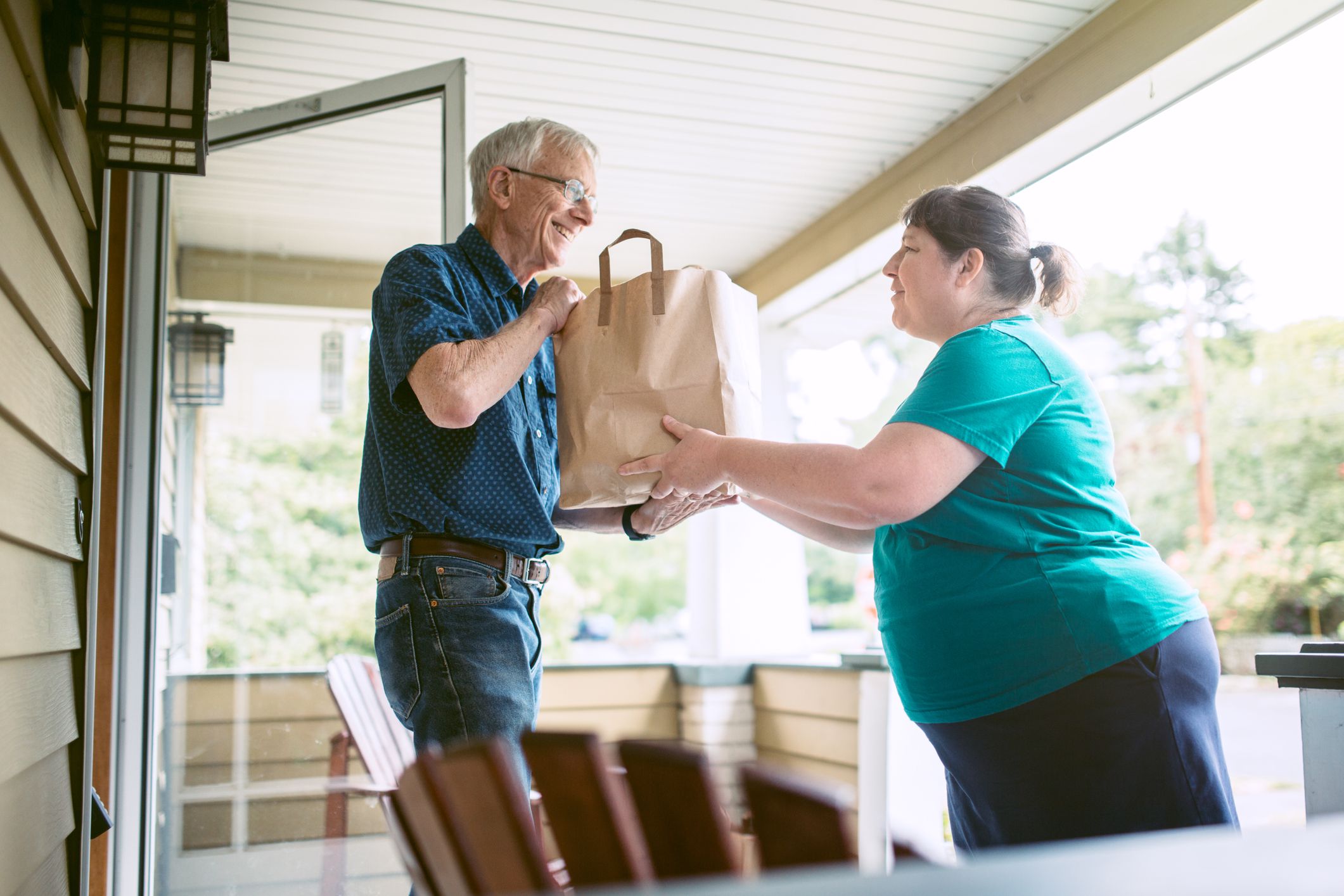 A kind and caring neighbor or friend delivers fresh produce from the grocery store to an elderly man at his home. He receives the gift with a smile on his face, grateful for the help and assistance. Horizontal image.