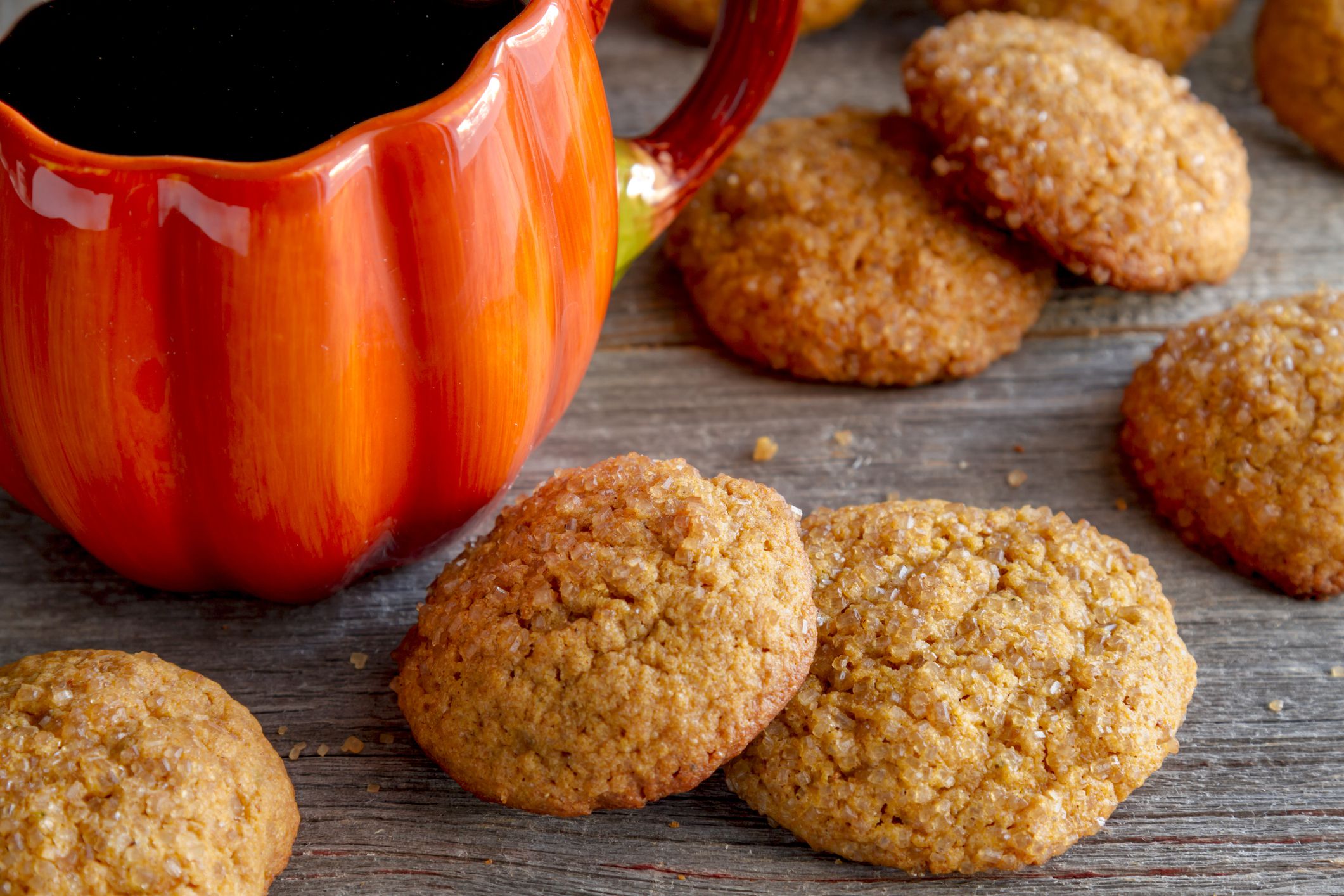 Fresh baked pumpkin spice cookies sitting on rustic wooden table with cup of coffee in pumpkin shaped mug