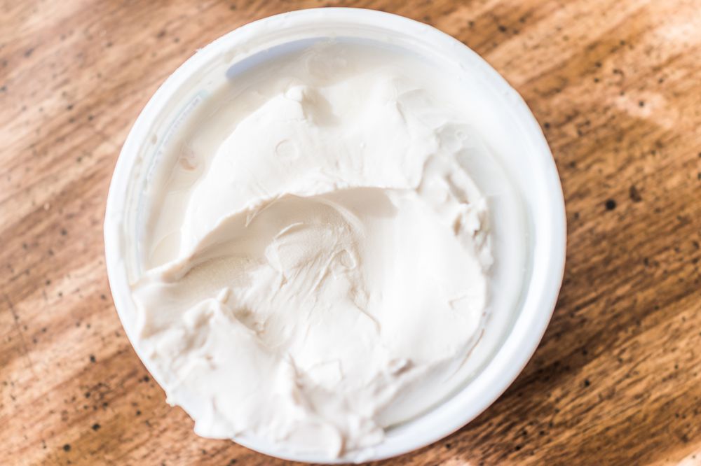 Closeup of small tub plastic container of white cream cheese on table, flat top view down macro
