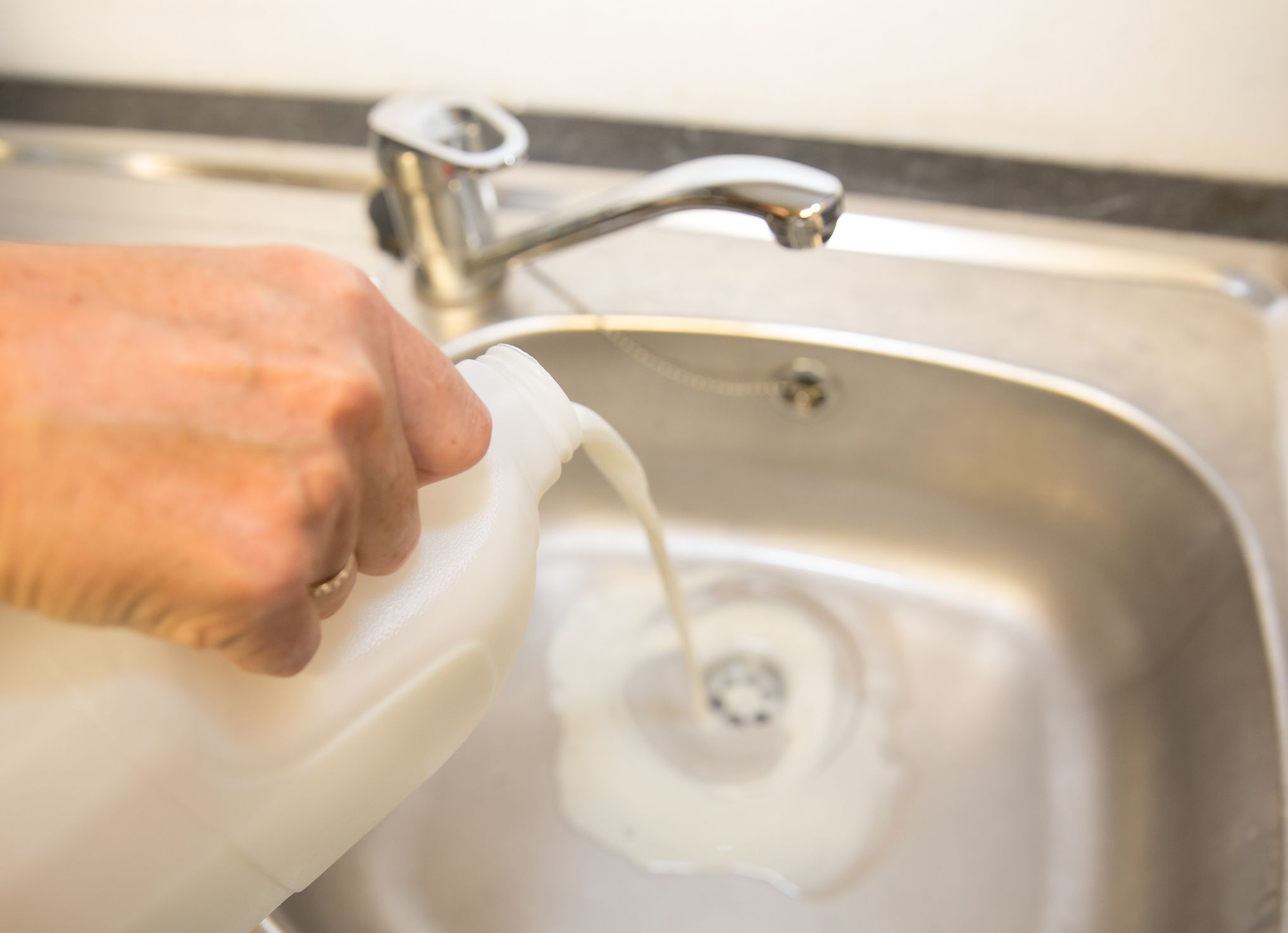Fresh milk being poured down a stainless steel sink - food products being wasted and milk farmers not achieving the price they need for sustainable production
