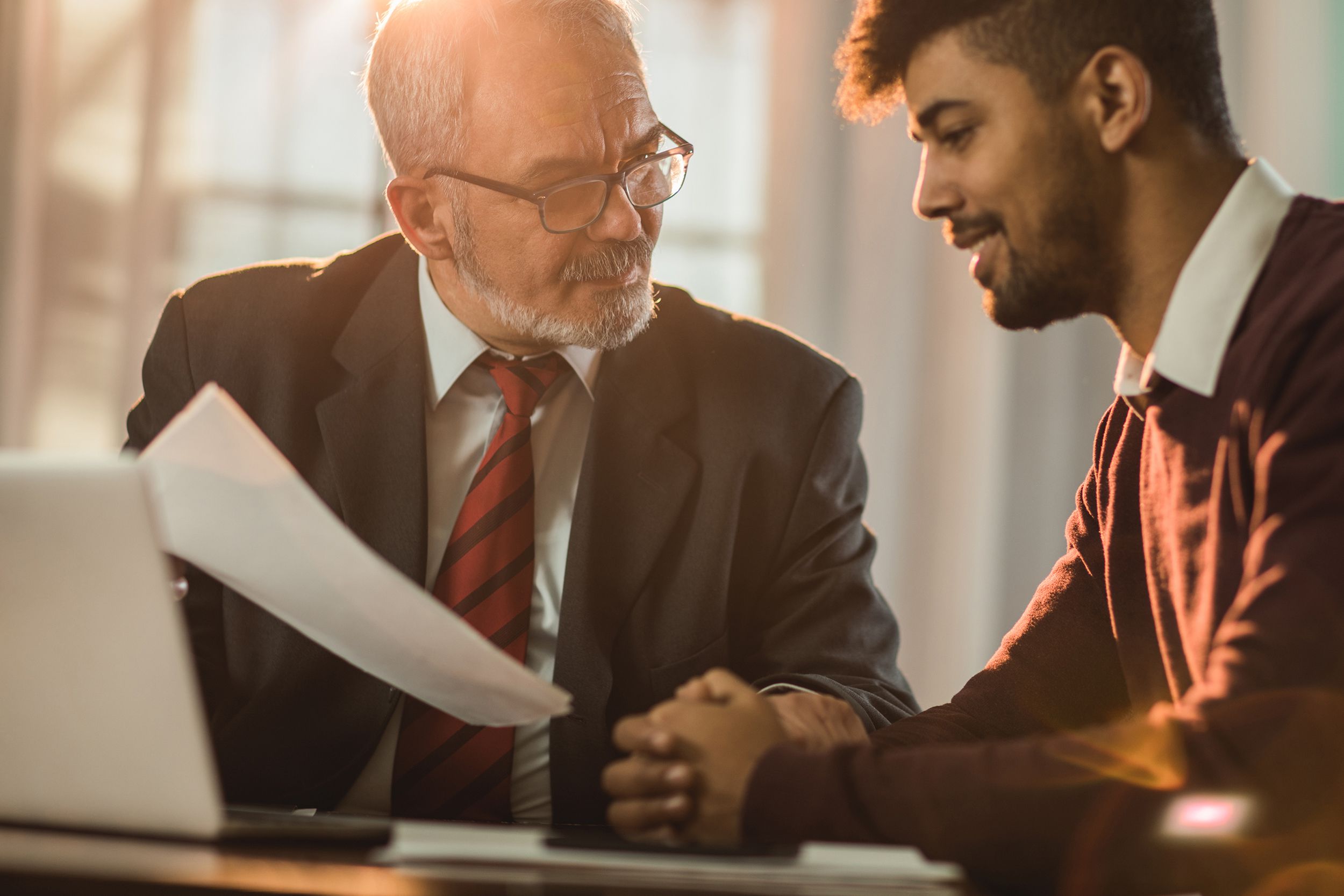 smiling insurance agent talking about paperwork with his young male customer in the office