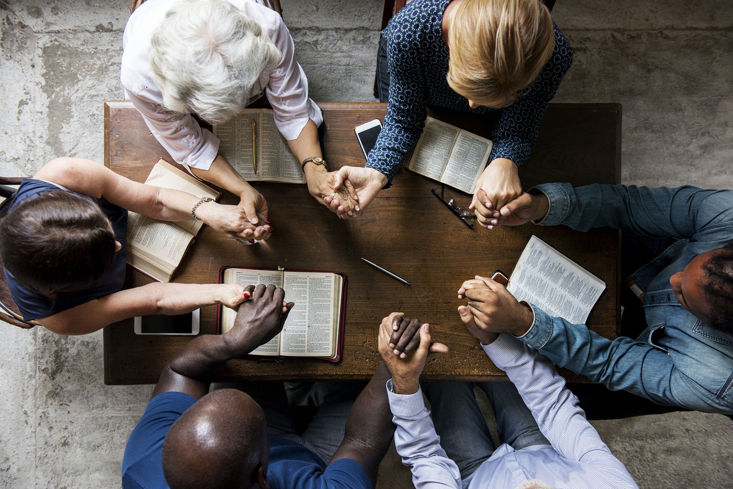 group of people holding hands praying together with bibles opened