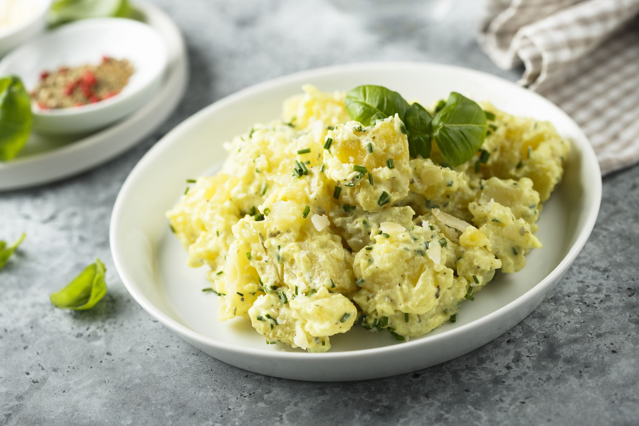 Classic southern style potato salad with herbs on a white bowl on a stone table with a blurred background of condiments