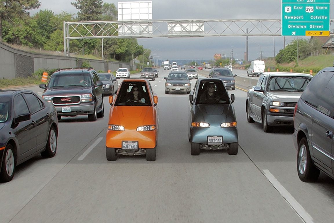 Two Commuter Tango Cars in one lane, orange and grey, in traffic on a motorway