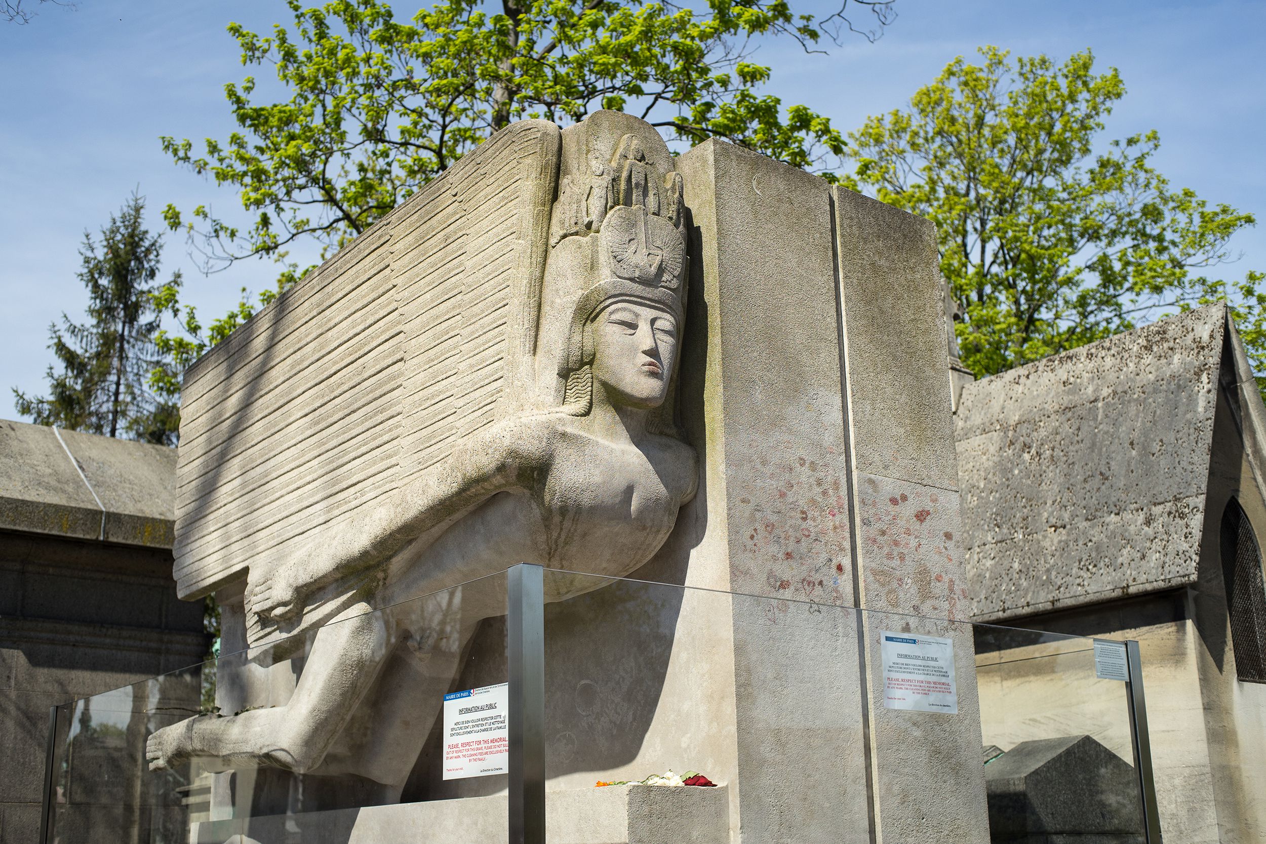 Grave of Oscar Wilde in the Pere Lachaise Cemetery, Paris, surrounded by a few other grave monuments, on a bright sunny day in late spring