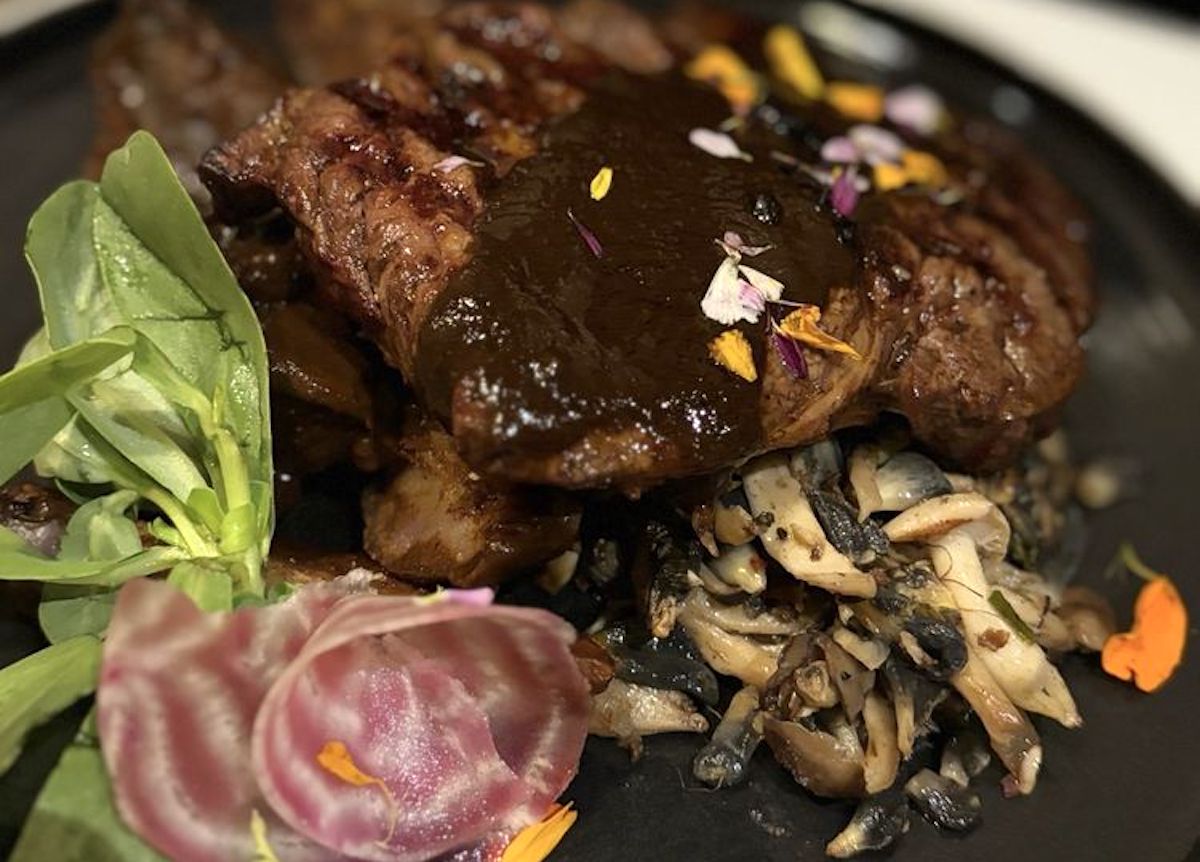 Grilled steak topped with dark sauce and edible flower petals, served with sautéed mixed mushrooms, fresh greens, and striped beetroot—an elevated dish inspired by top cheap steak restaurants.