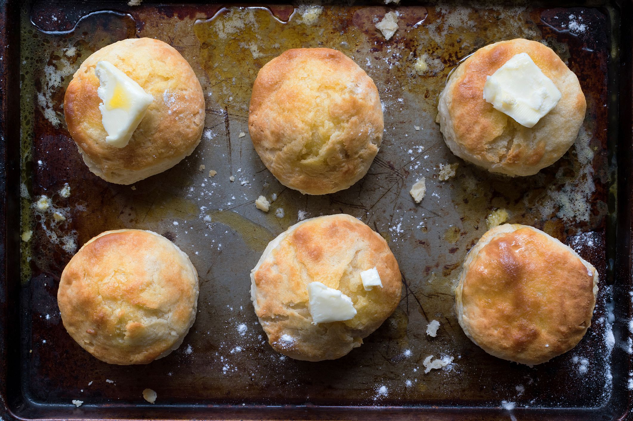 Top view of six biscuits with scallion butter equally positioned on a baking pan, three have slices of butter, image is size of the baking pan