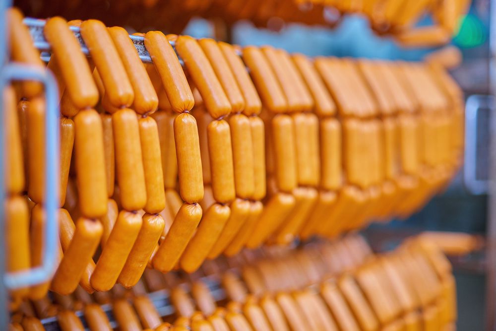 Raw sausages on racks in storage room at meat processing factory