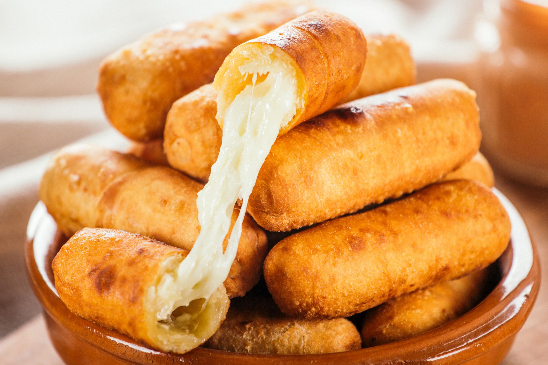 tequeños stacked in bowl with melted cheese dripping out