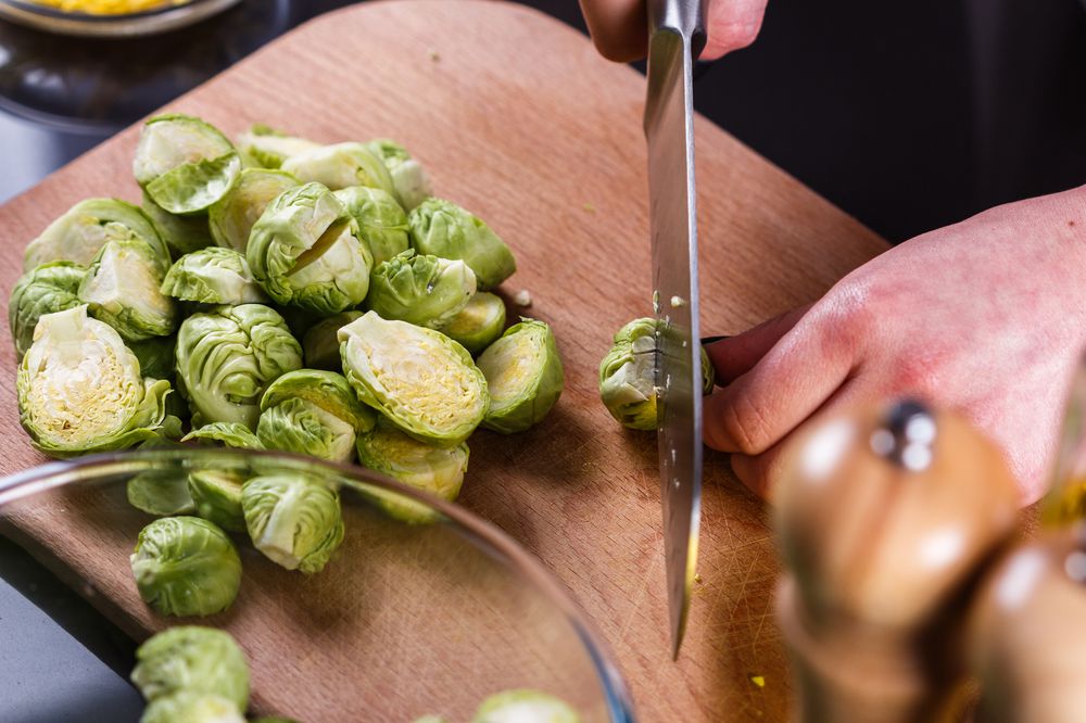 young woman cuts Brussels sprouts on a wooden cutting board