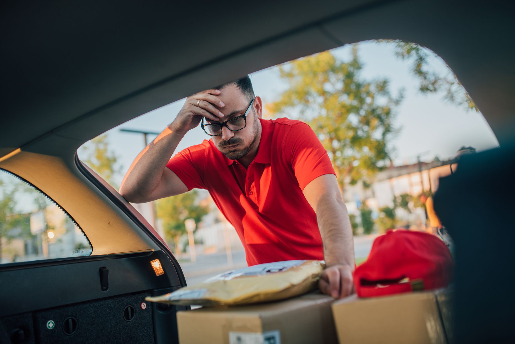 A delivery man under a mild stress looking for a certain package at the back of his car, worries about the delivery time