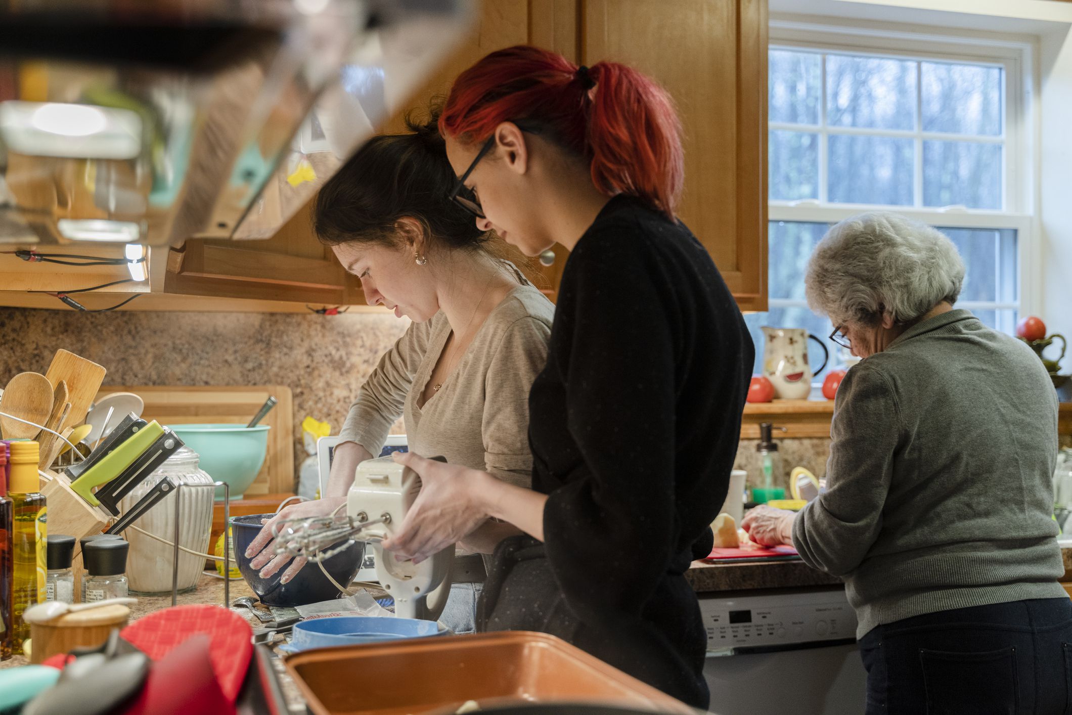 Teenage girl helping her older sister mix the pie batter by holding the mixing bowl as they both cook during quarantine.