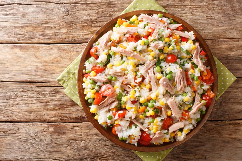 Salad of rice, tuna, tomatoes, sweet pepper, corn, green peas and herbs close-up in a plate. horizontal top view