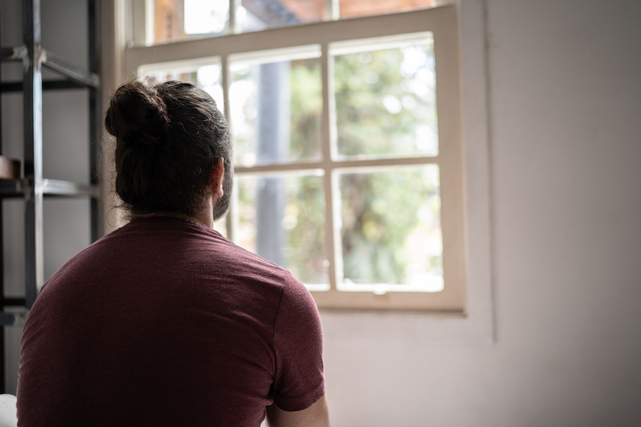 Rear view of a man looking through the window at home