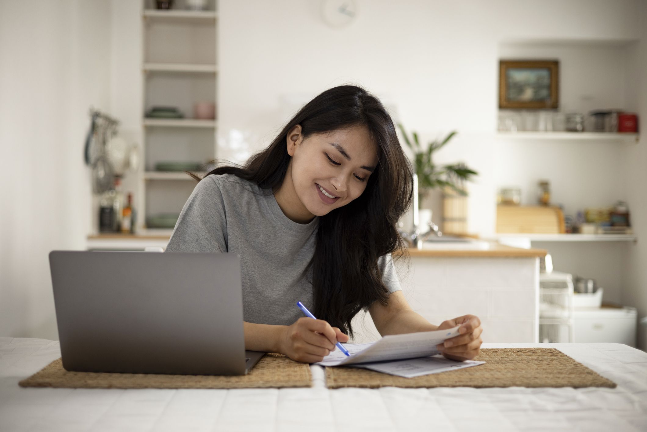 Young woman of a Mongolian ethnicity, doing her taxes and sorting out her finances at home, using a laptop