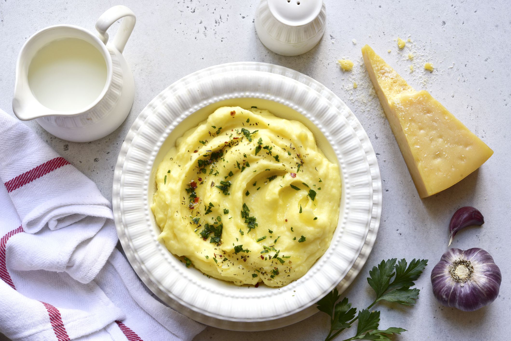 Mashed potato with parmesan cheese and herb in a white bowl on a light slate, stone or concrete background. Top view with copy space.