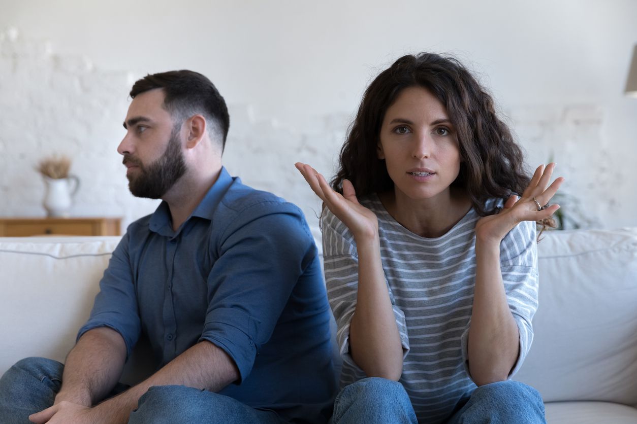 A couple sitting on a couch having an argument while the male partner turns away.