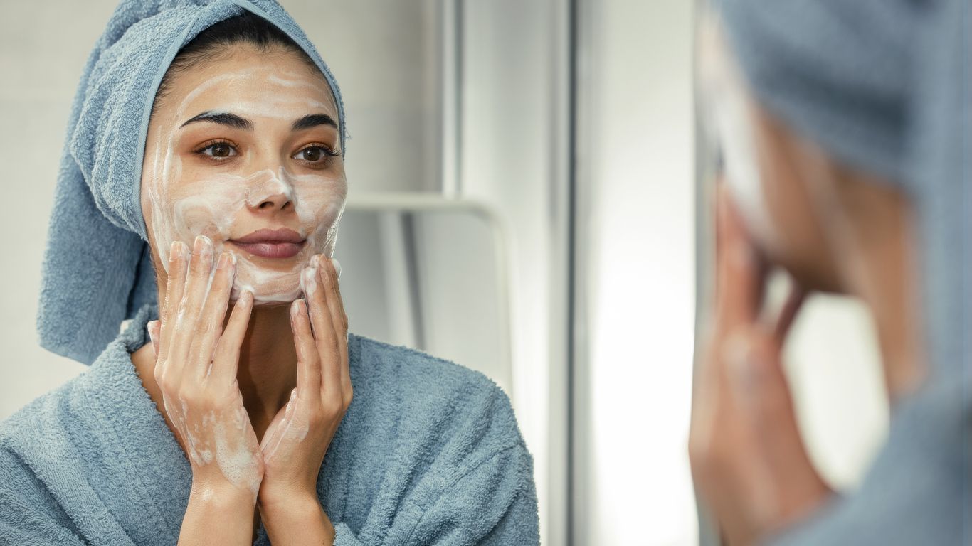 A woman in blue towels applying nice lotion to her face.