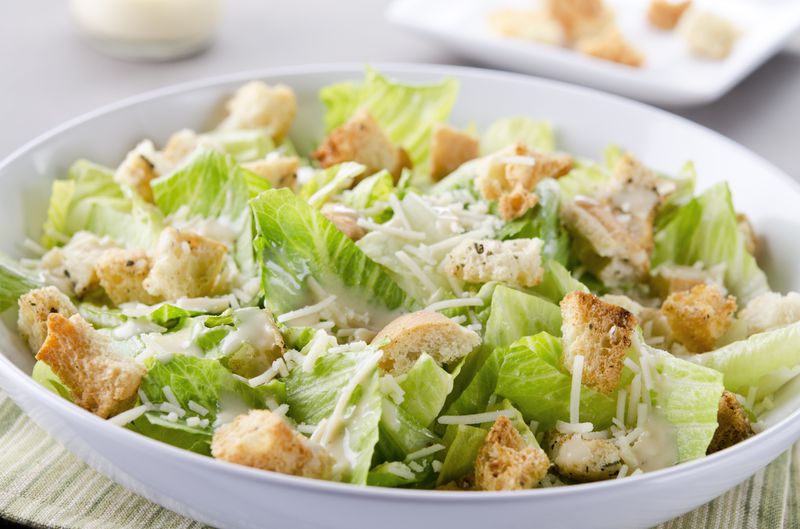 A bowl of Caesar Salad with croutons and cheese on table