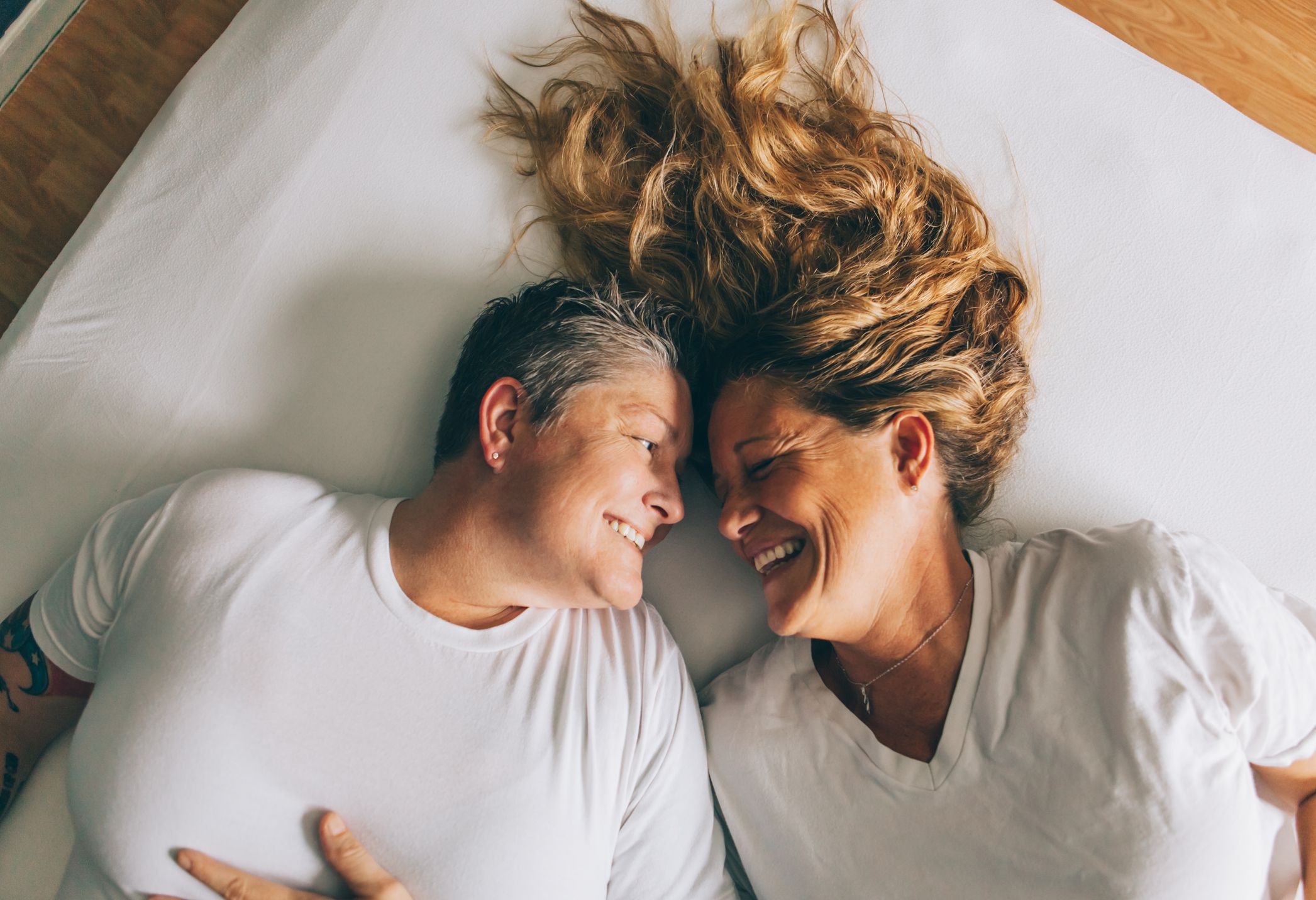 Lesbian couple joyfully laughing while laying in bed.